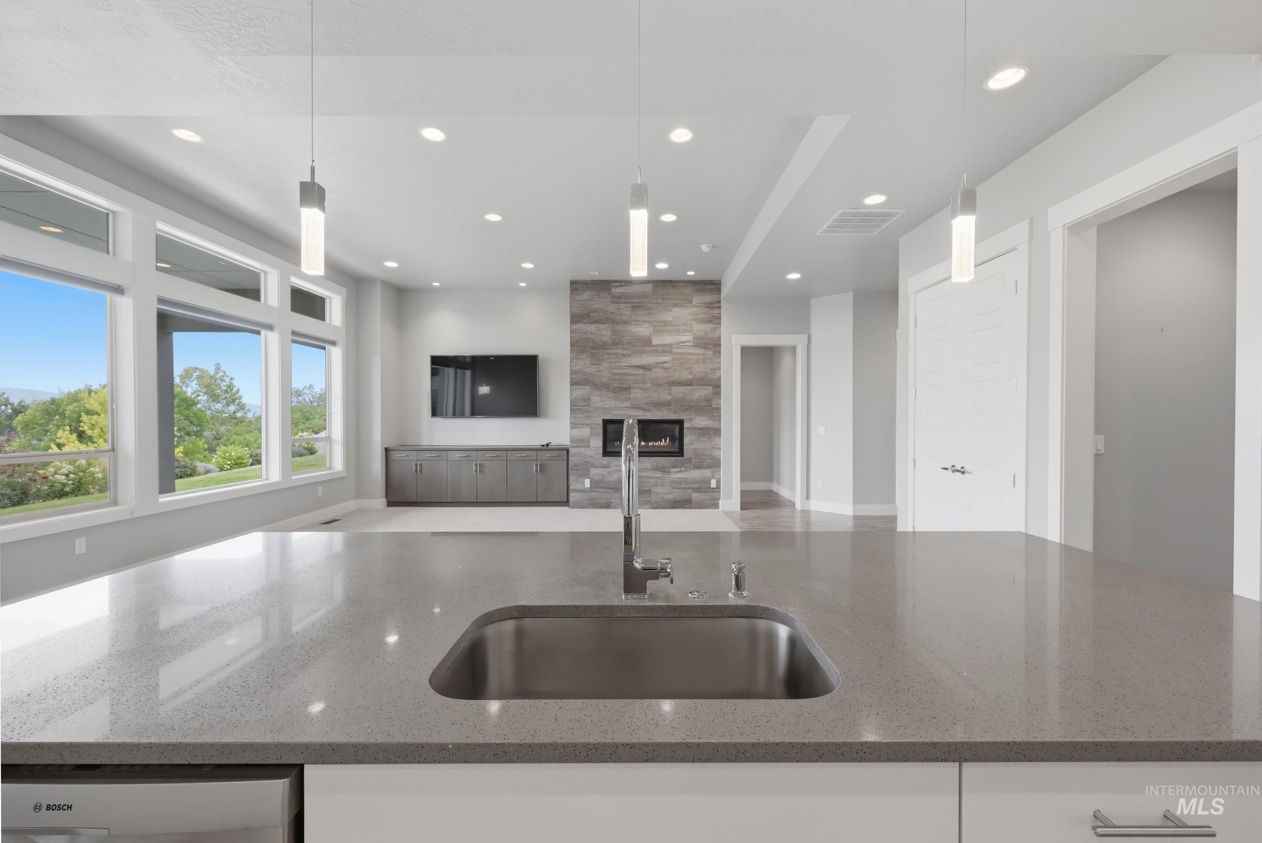 Spacious open-concept interior featuring a large kitchen island with an undermount stainless steel sink, a stone-faced fireplace, extensive window framing, recessed lighting, and pendant fixtures