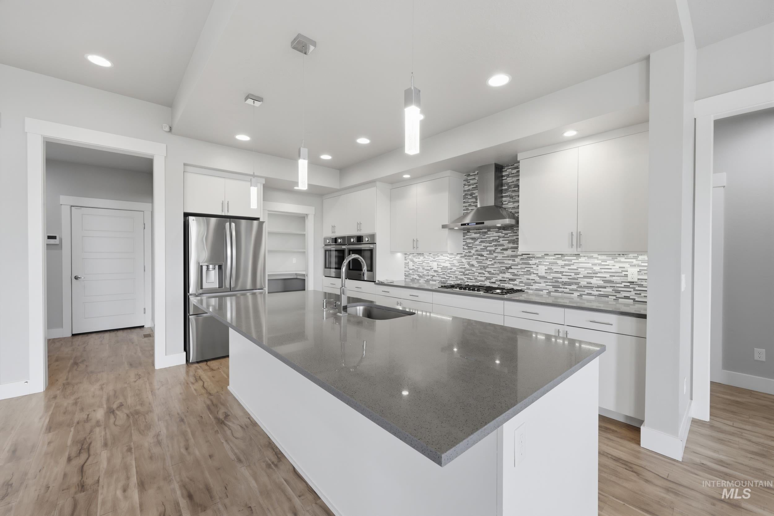 Kitchen featuring a large center island with integrated sink, stainless steel appliances, a tiled backsplash, recessed lighting, and wood-finish flooring