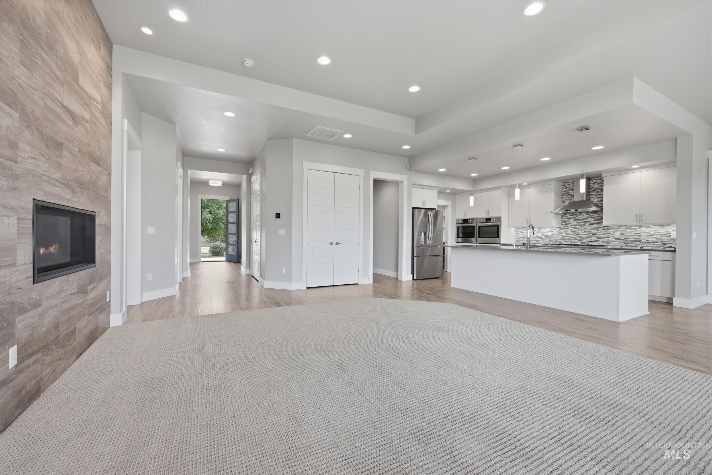 Open-concept living area featuring a built-in fireplace with a stone-finish facade, recessed lighting, and wood-finish flooring