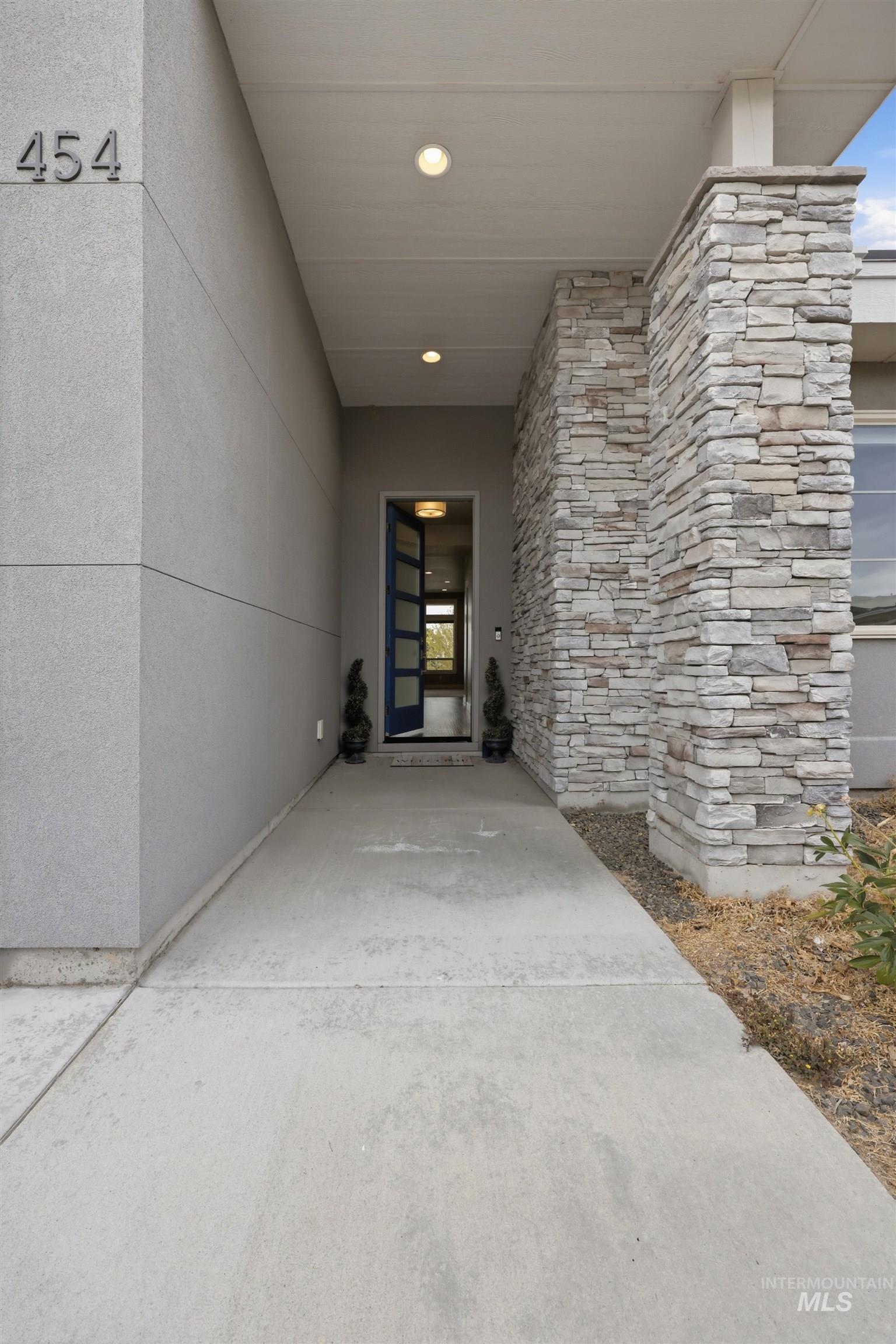 Covered entryway featuring a modern front door with sidelights, stacked stone column, smooth stucco exterior, and recessed lighting