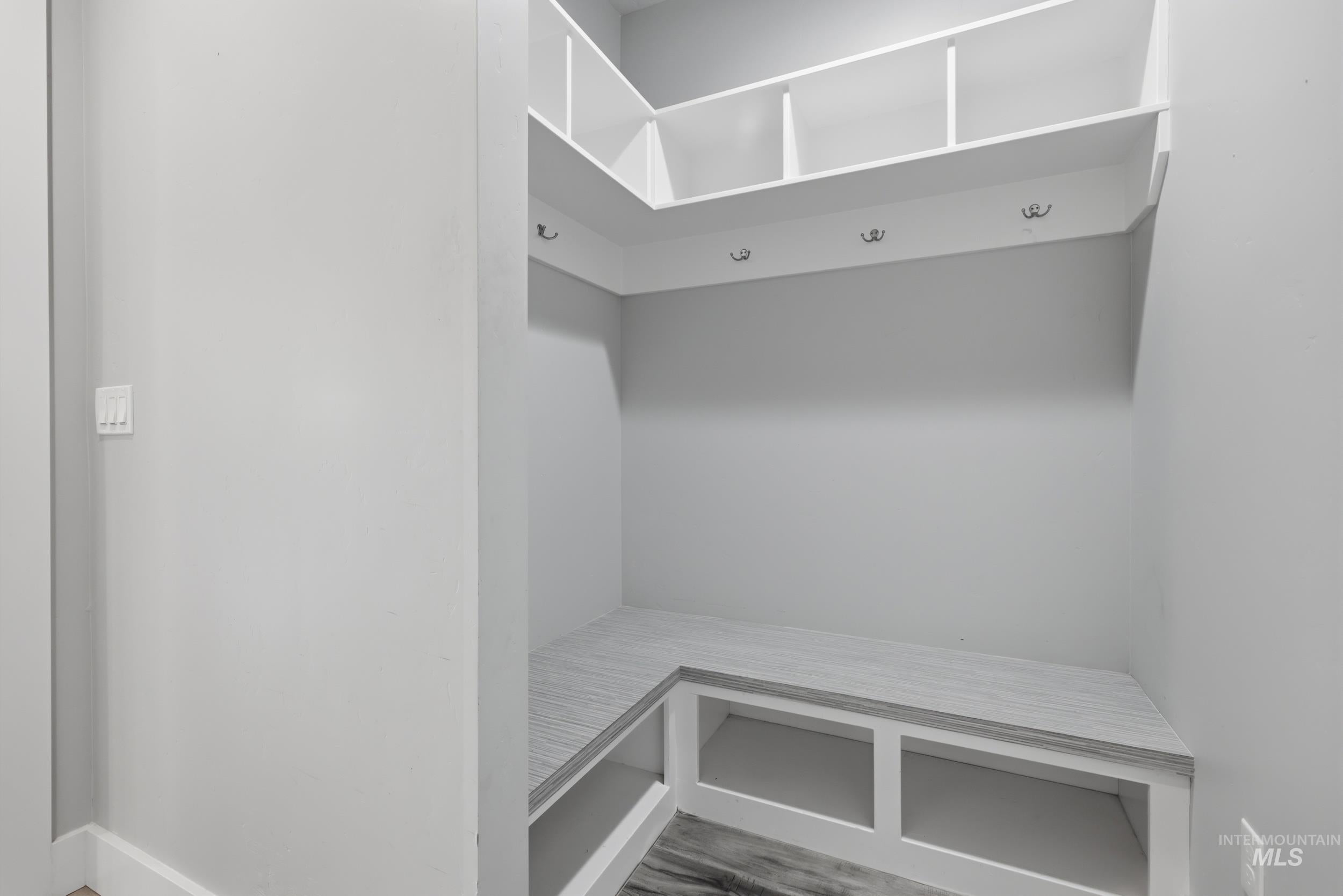 Built-in mudroom bench with cubbies, overhead shelving, and wall-mounted hooks, all finished in a light neutral palette