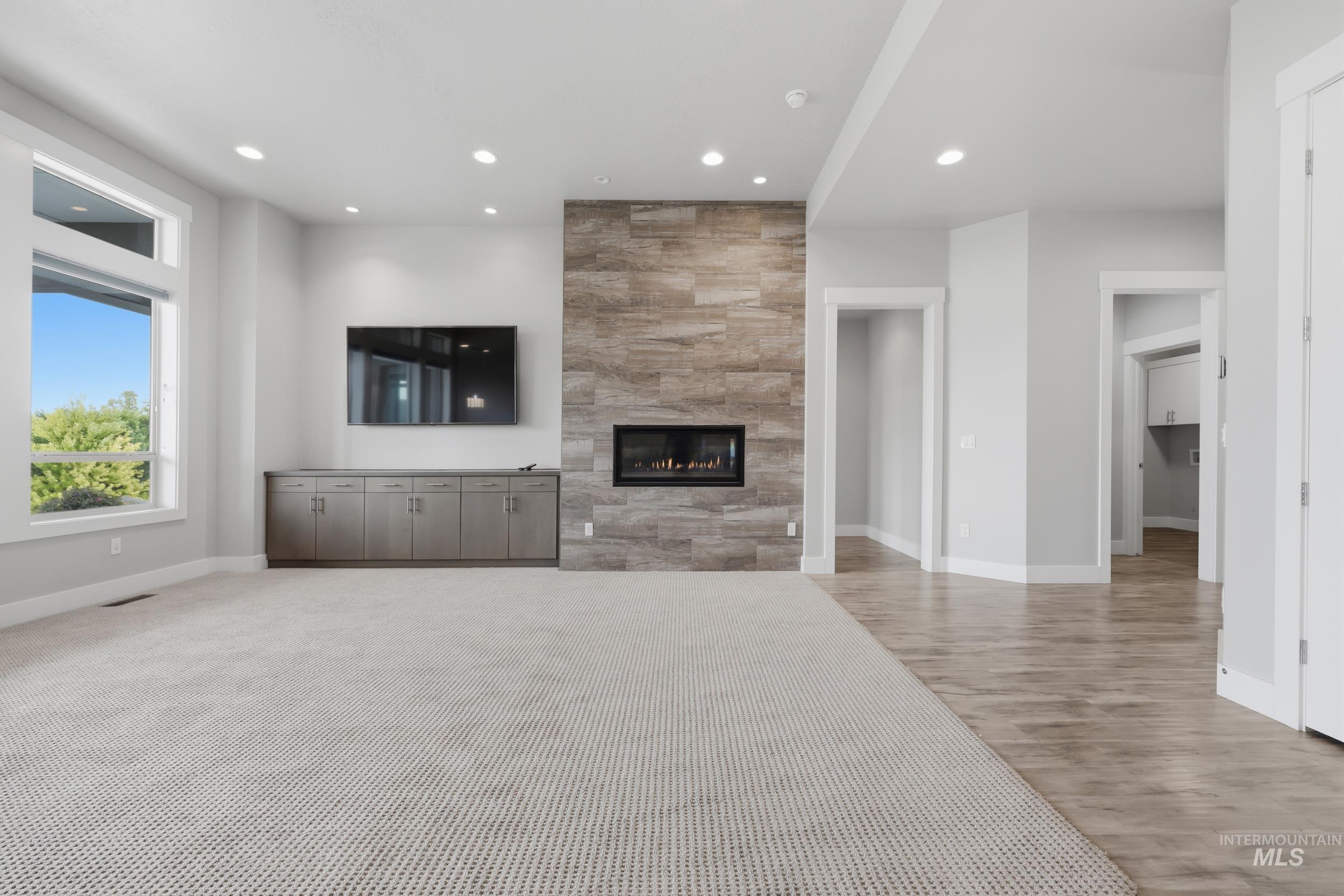 Spacious living area featuring a contemporary fireplace with stone surround, built-in cabinetry, large picture windows, recessed lighting, and a combination of plush carpeting and wood-finish flooring