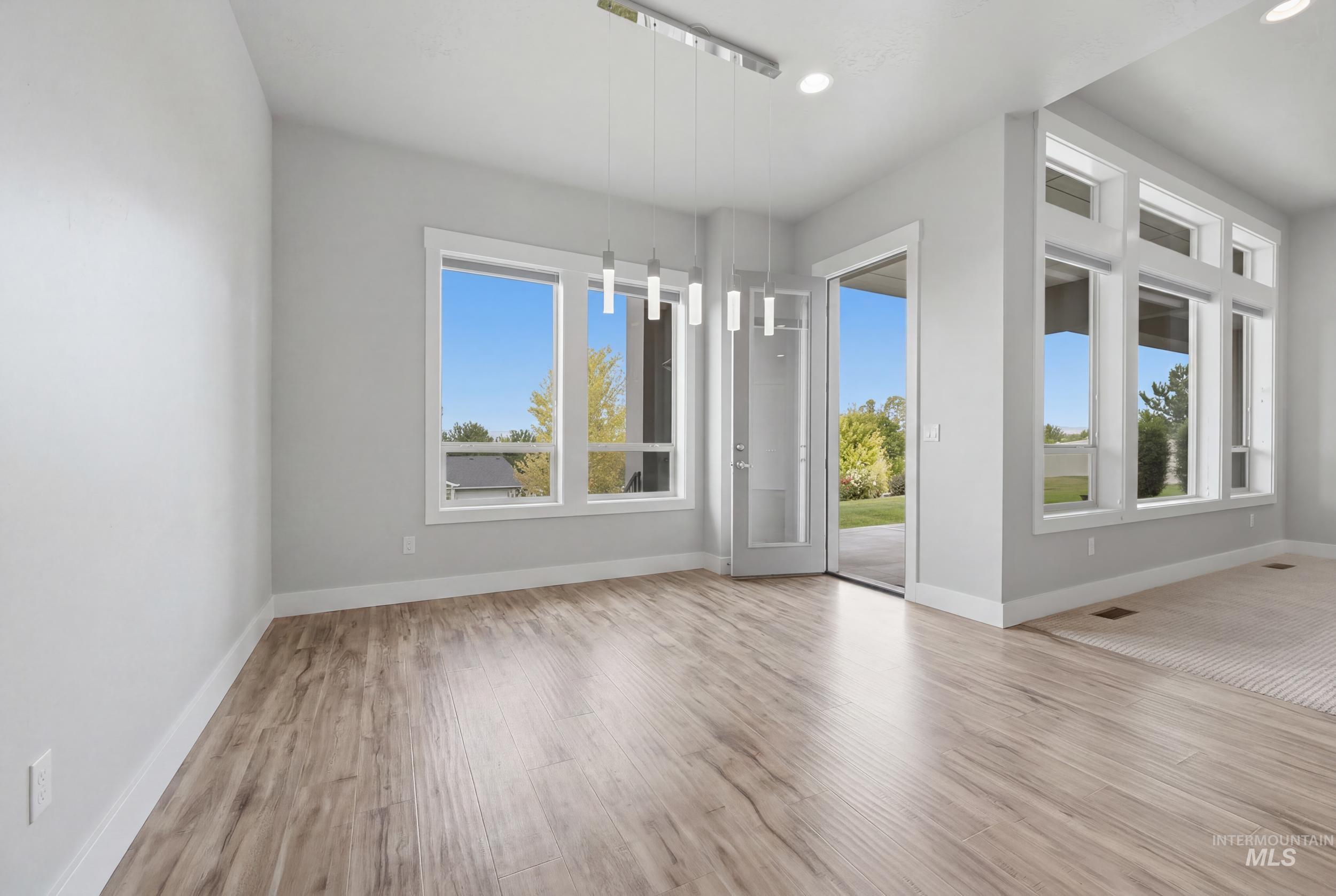 Open-concept living area featuring wood-finish flooring, a modern linear pendant light fixture, multiple large windows, and a glass-paneled door providing direct exterior access