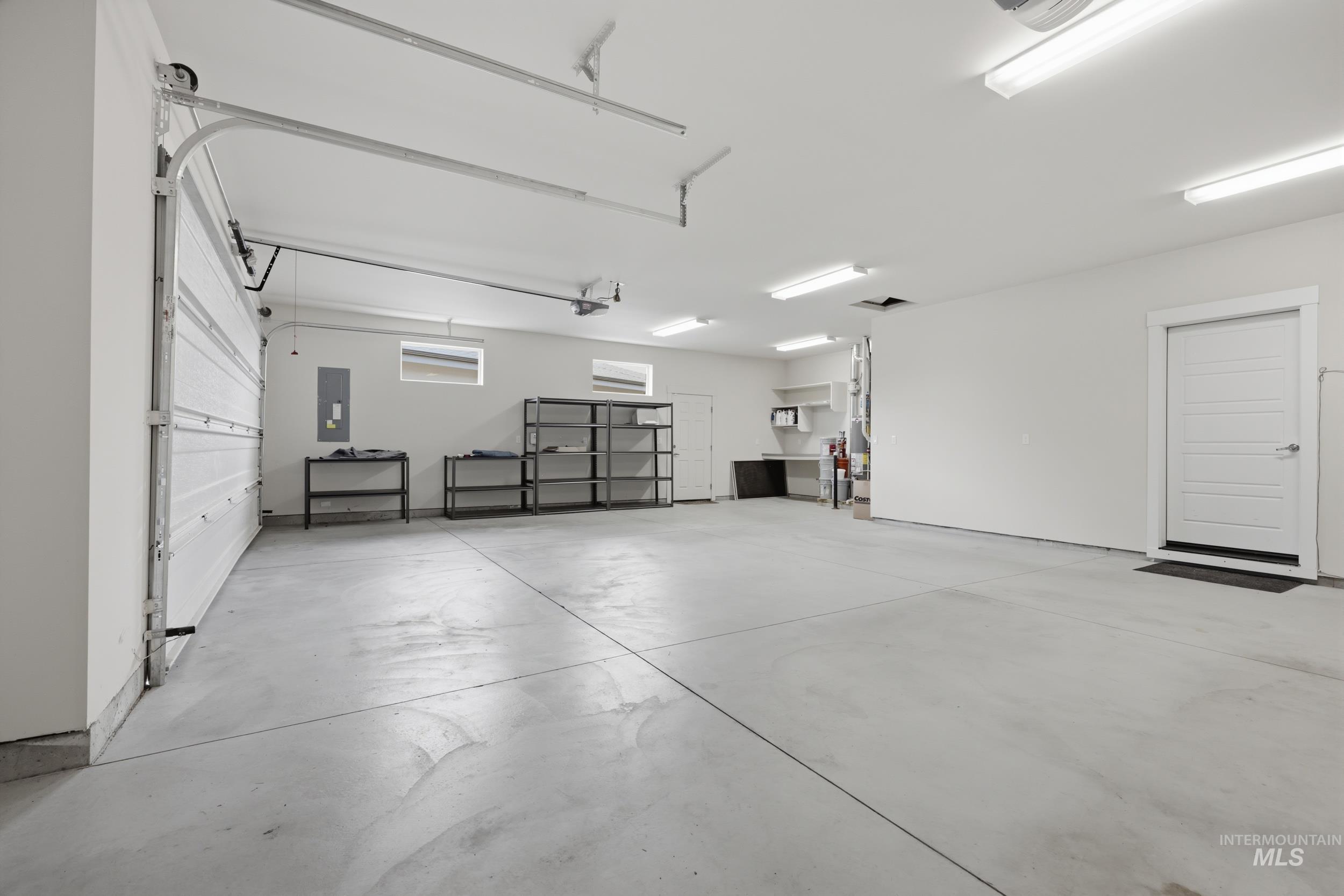 Spacious garage featuring a concrete floor, bright overhead lighting, multiple windows, a sectional garage door, and a paneled interior door