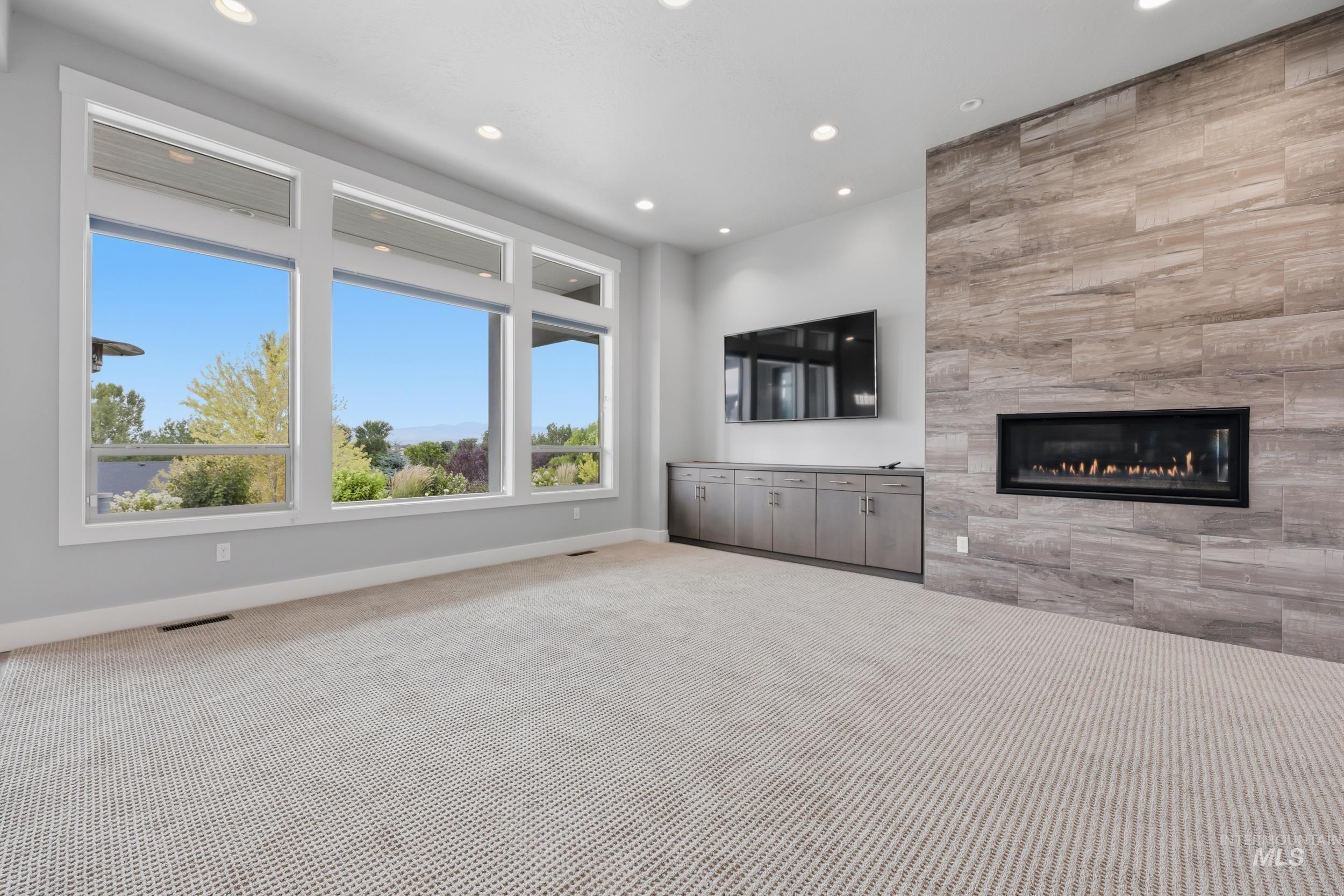 Spacious room featuring a wall of windows, a linear fireplace with stone-look surround, recessed lighting, and built-in cabinetry