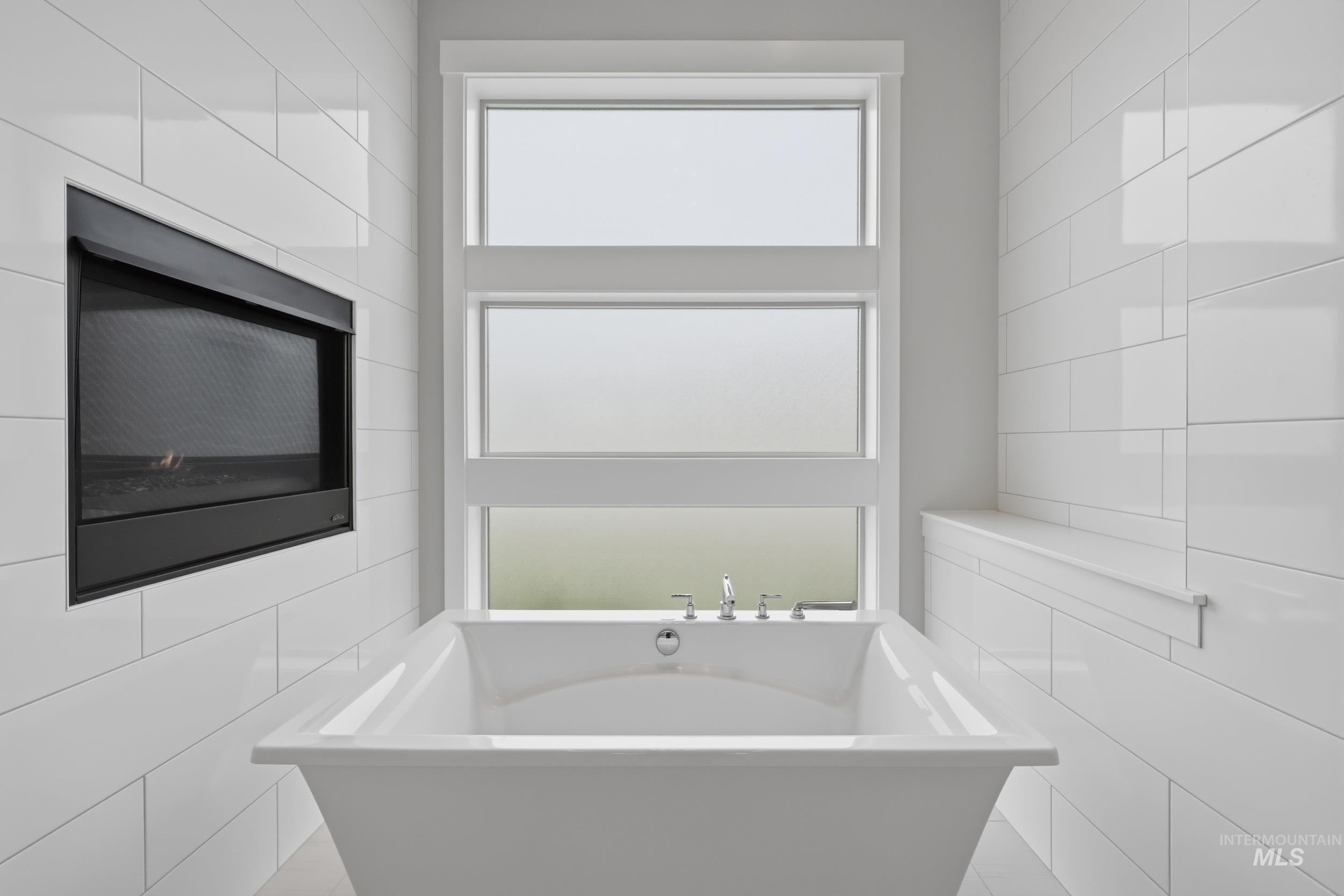 Freestanding soaking tub with polished chrome fixtures, set against white subway tile walls