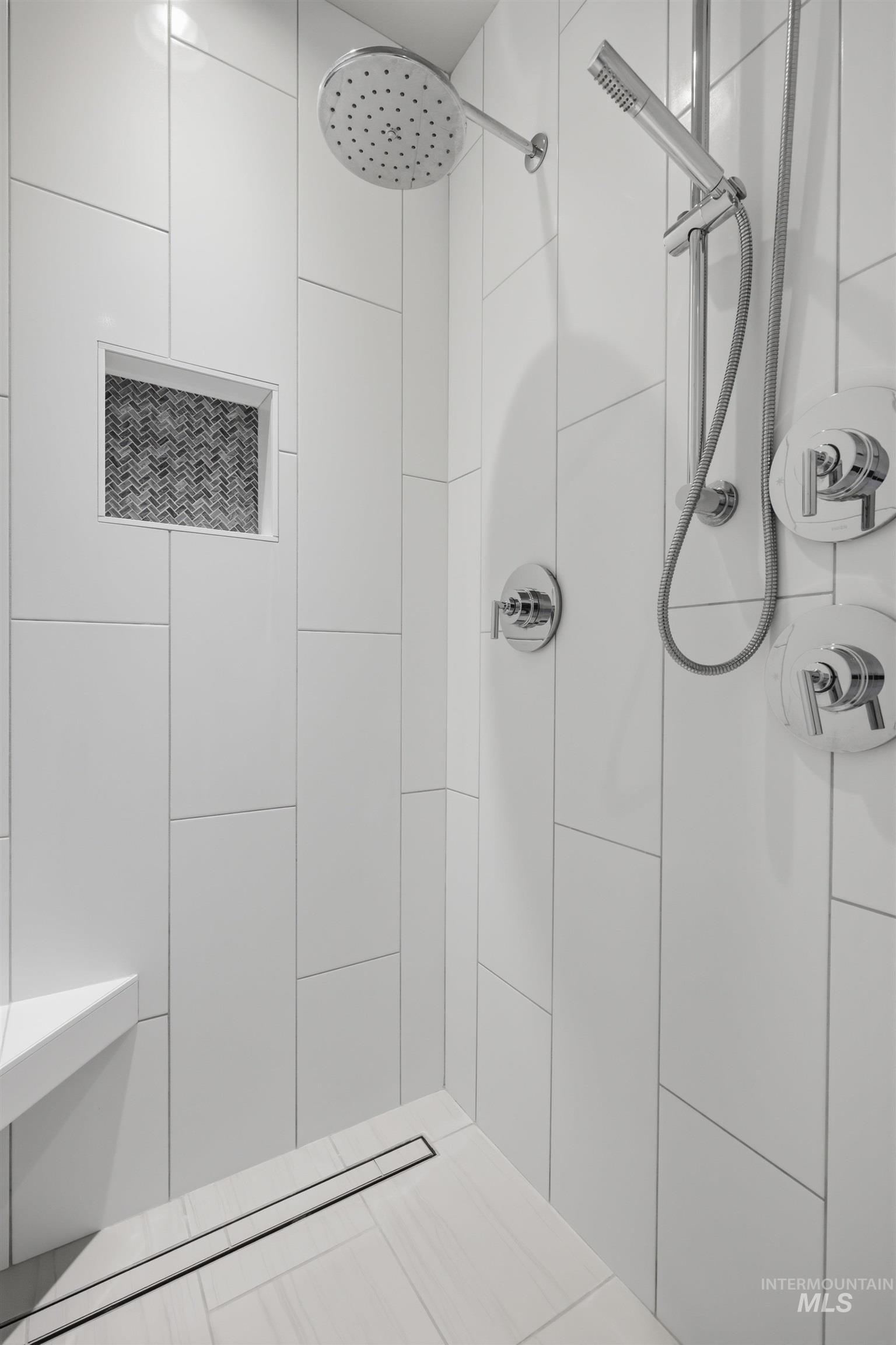 Tiled shower featuring a rainfall showerhead, handheld spray, built-in bench, linear drain, and recessed niche with mosaic tile