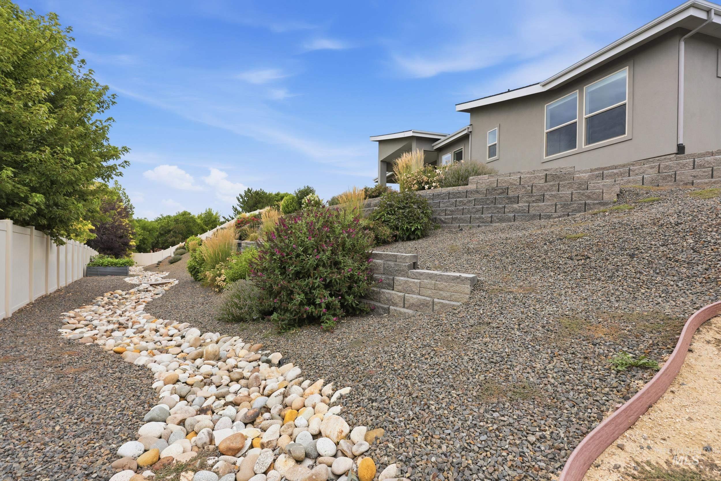 Landscaped exterior featuring a decorative rock riverbed, gravel hardscaping, and tiered retaining walls