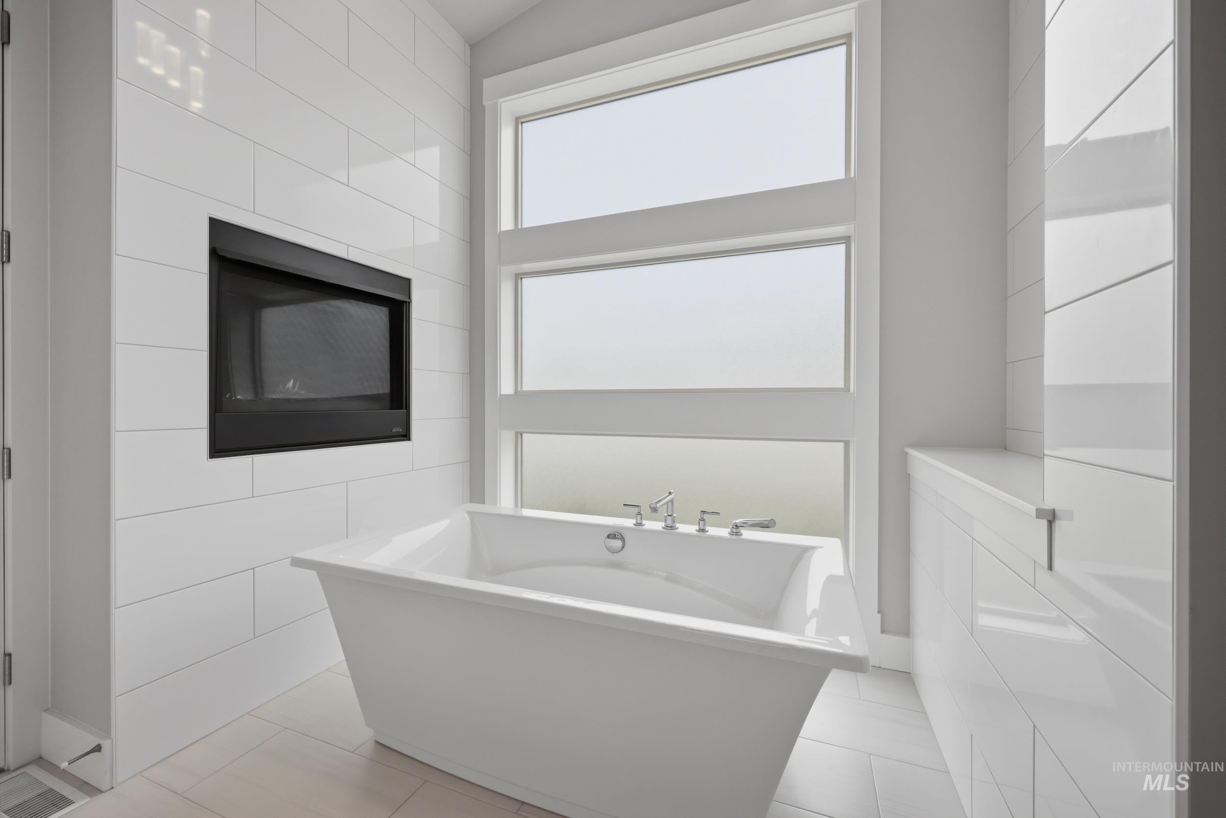 Freestanding soaking tub with chrome fixtures, set against a backdrop of white subway tile