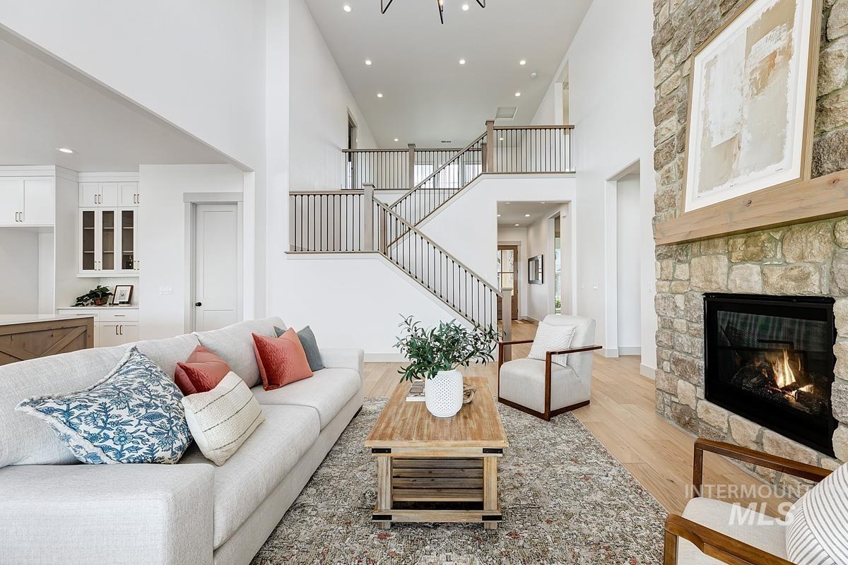 Living room featuring a high ceiling, light wood finished floors, recessed lighting, a fireplace, and stairs