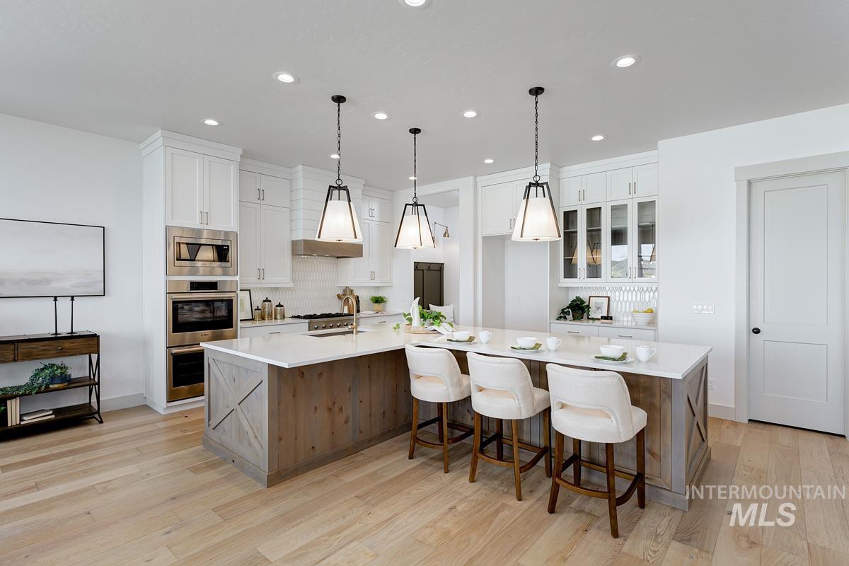 Kitchen with white cabinets, a breakfast bar area, a large island with sink, recessed lighting, and decorative backsplash