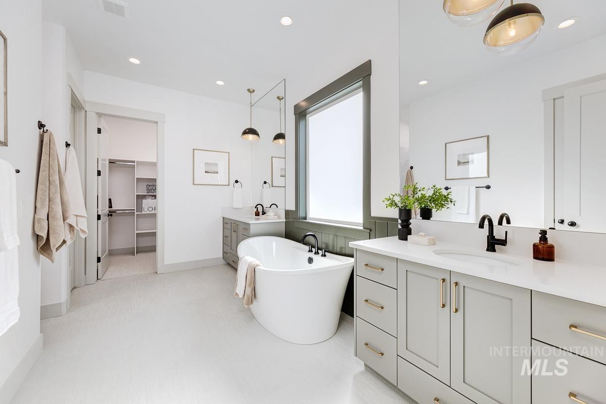 Bathroom featuring a freestanding tub, two vanities, a walk in closet, and recessed lighting