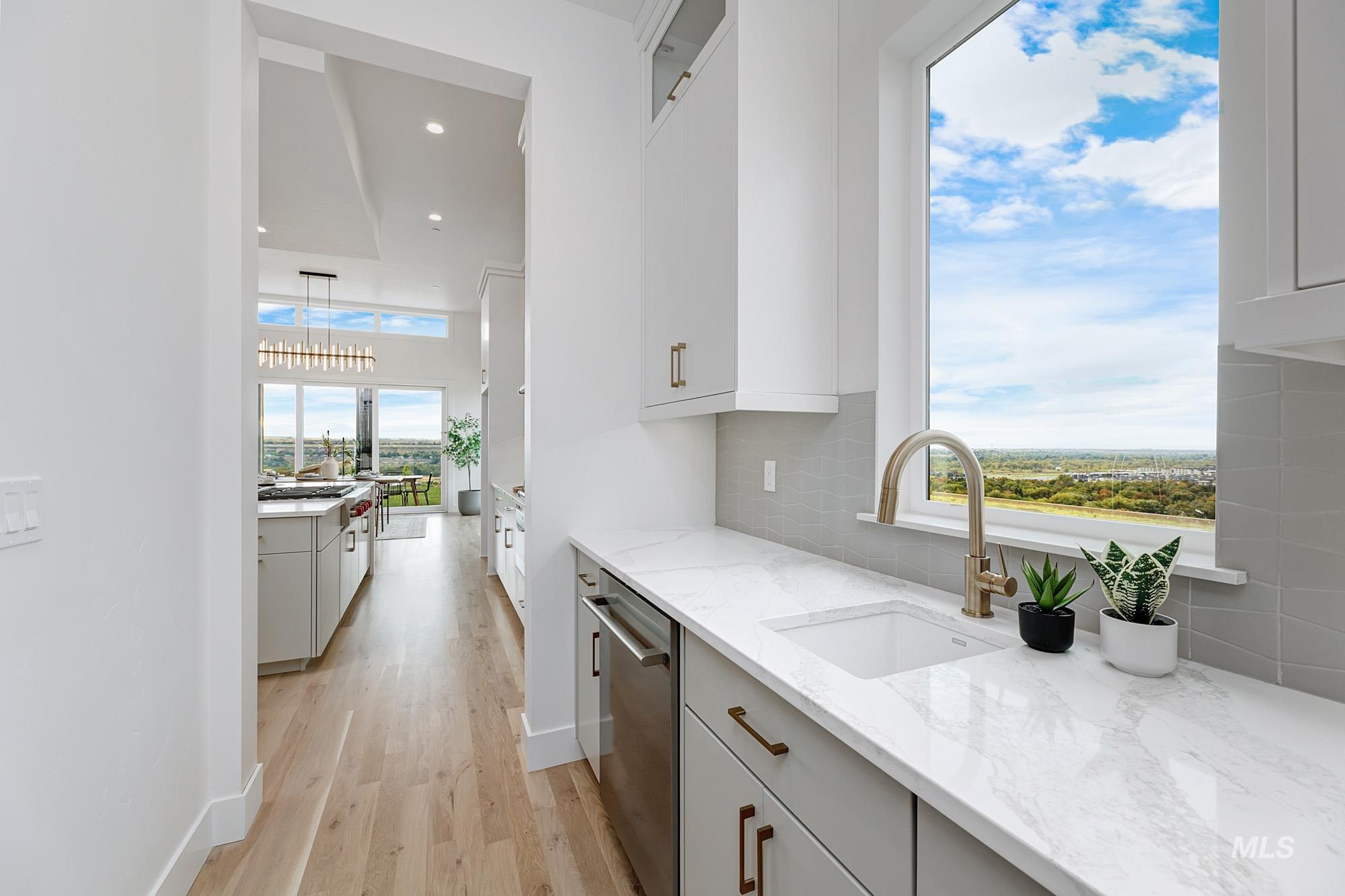 Kitchen with light stone countertops, light wood-style flooring, white cabinetry, stainless steel dishwasher, and backsplash