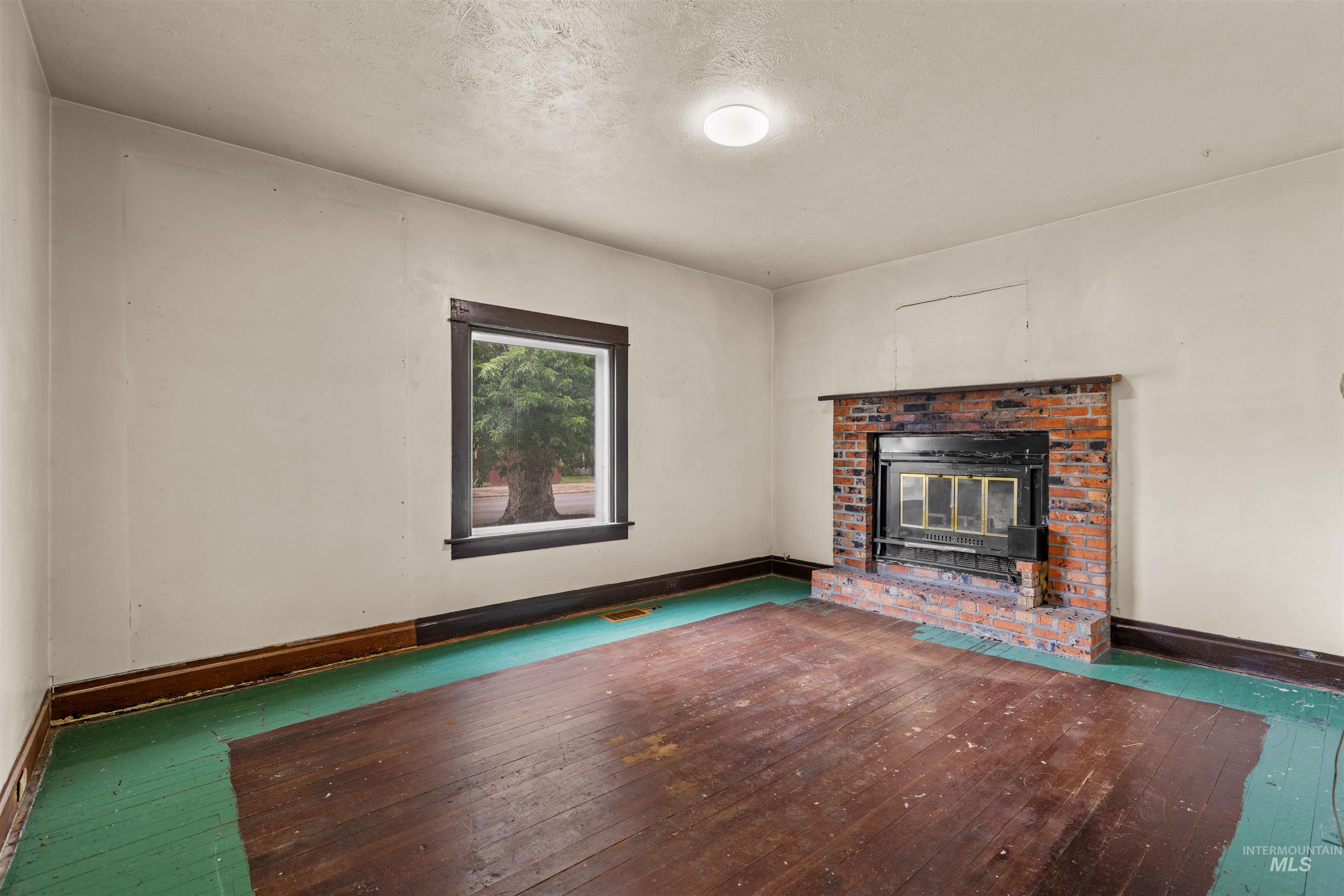 Spacious room featuring a brick fireplace with a black insert, a window with dark wood trim, and a ceiling-mounted light fixture