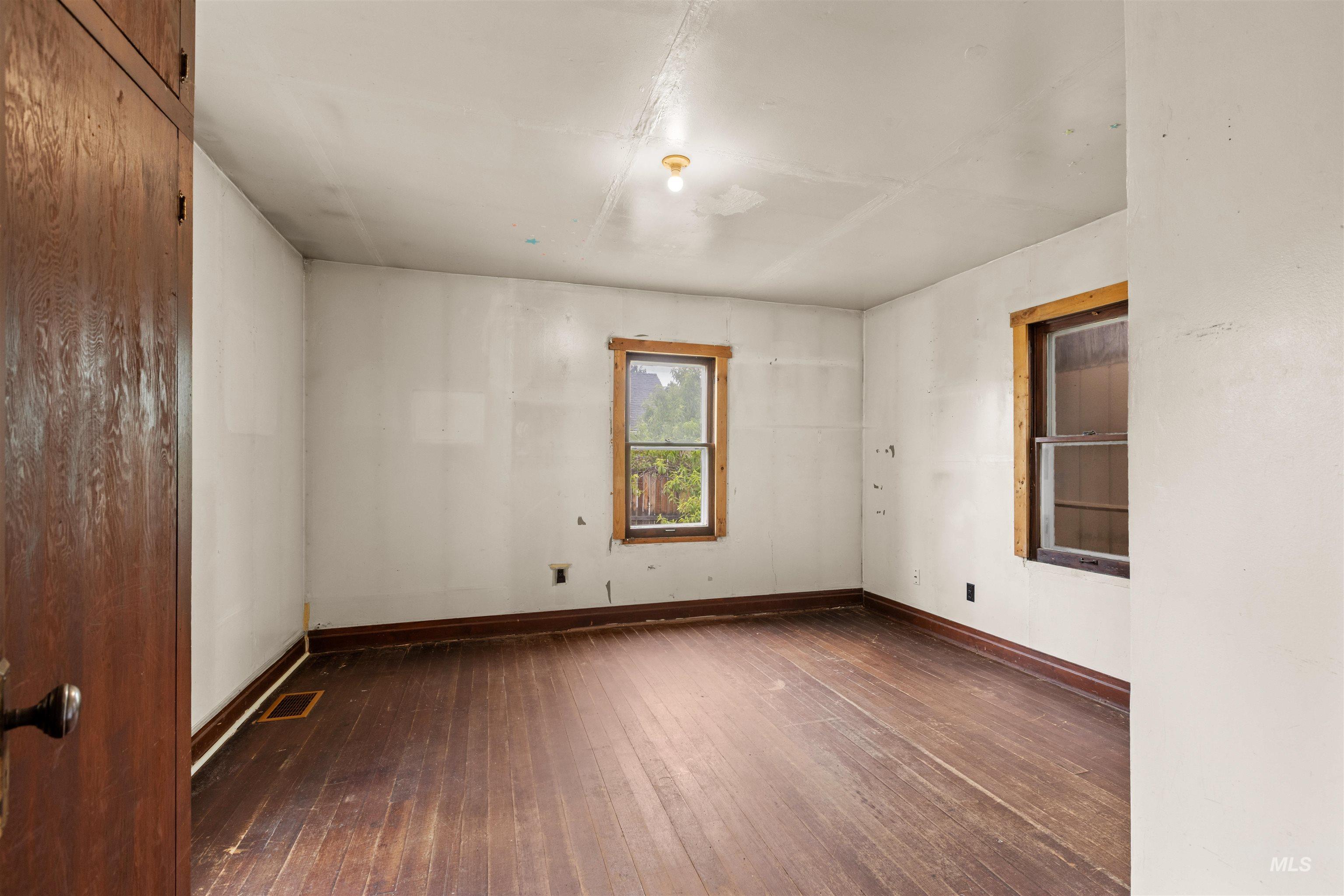 Room featuring wood-finish flooring, two windows with wood trim, and a ceiling-mounted light fixture