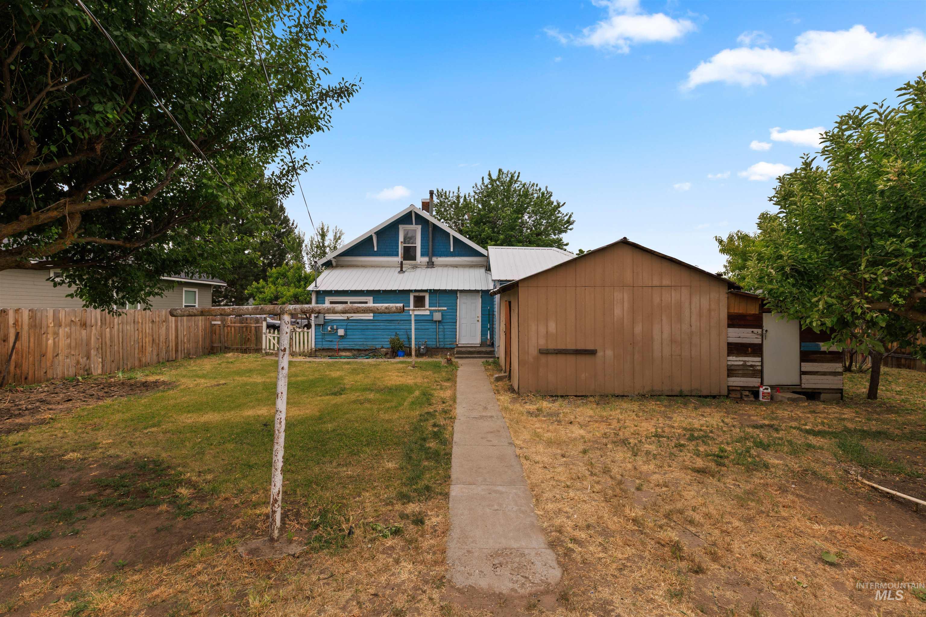 Expansive backyard featuring a concrete pathway, a separate storage structure, and mature trees