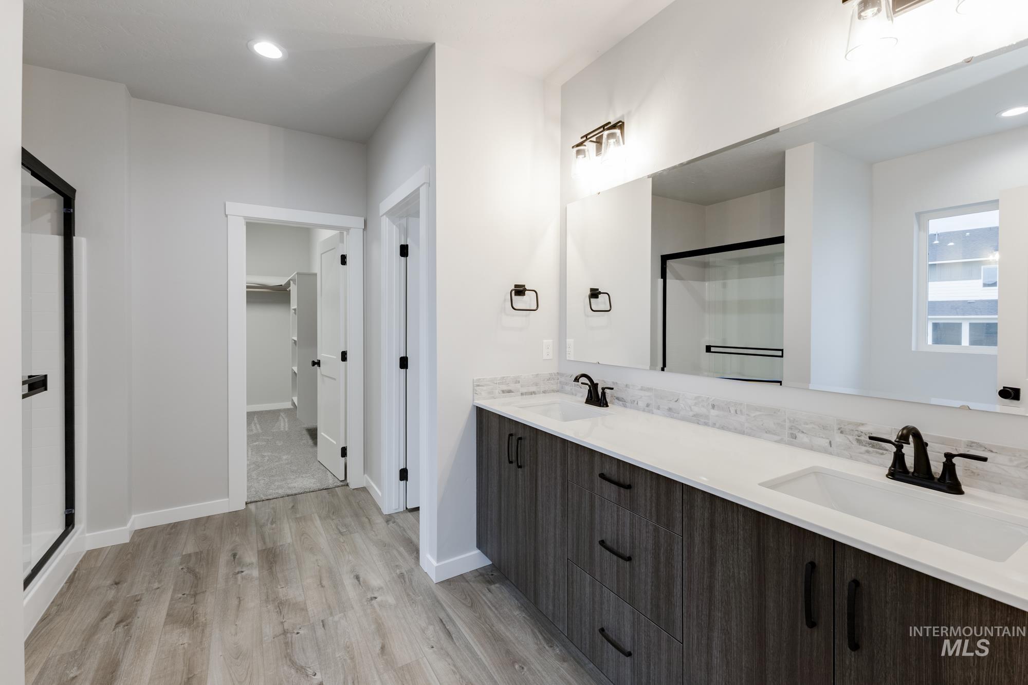 Bathroom with a shower stall, double vanity, a walk in closet, light wood finished floors, and recessed lighting