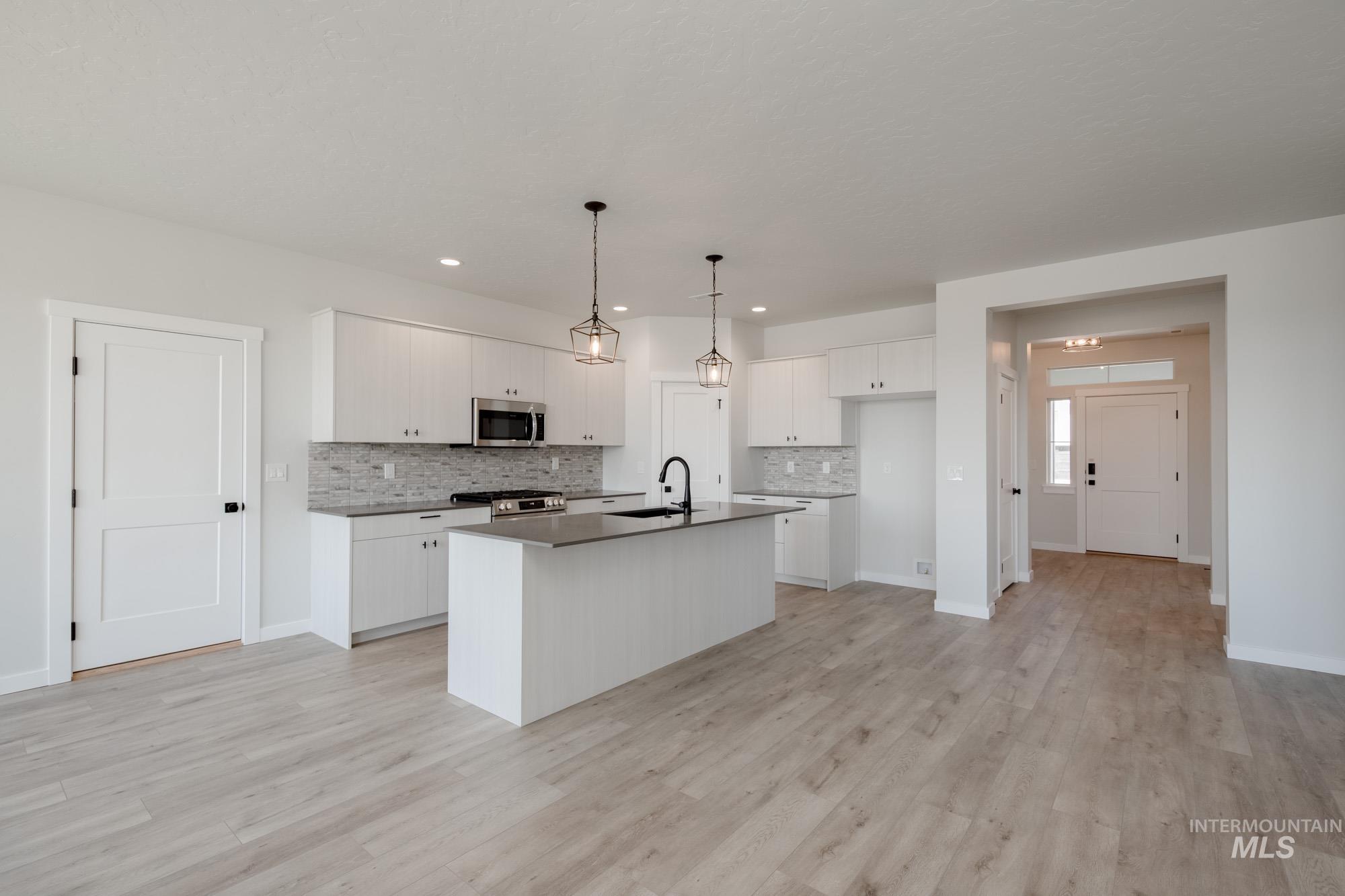 Kitchen with tasteful backsplash, decorative light fixtures, white cabinets, and light wood-style floors