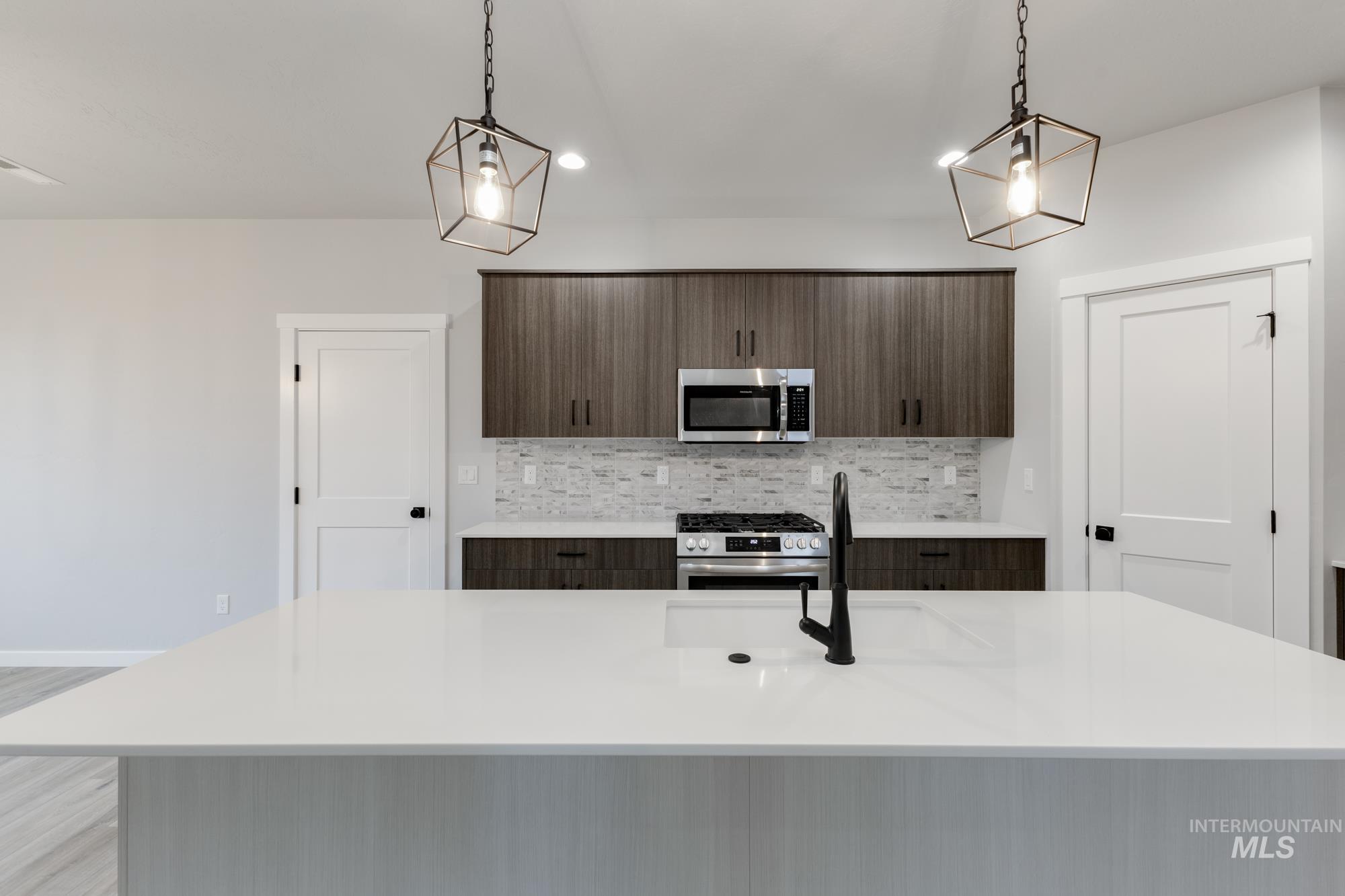 Kitchen featuring a kitchen island with sink, stainless steel appliances, modern cabinets, light stone counters, and pendant lighting