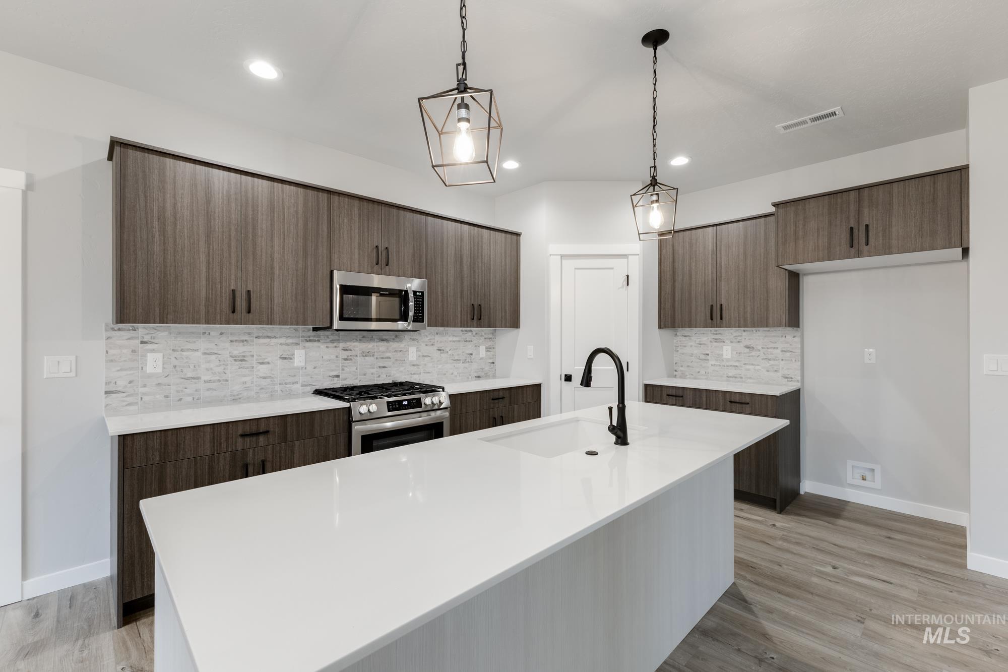 Kitchen with hanging light fixtures, stainless steel appliances, modern cabinets, a center island with sink, and recessed lighting