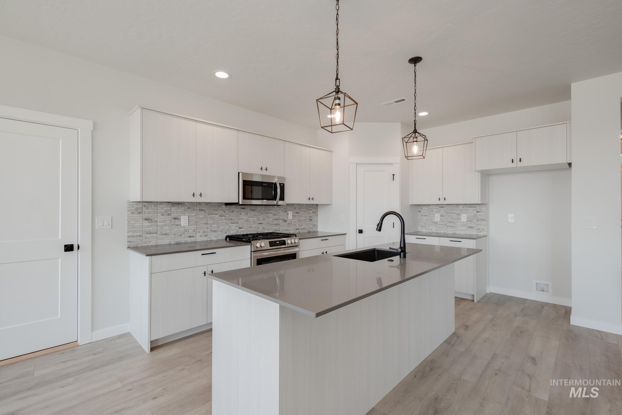 Kitchen with appliances with stainless steel finishes, a center island with sink, light wood-type flooring, pendant lighting, and tasteful backsplash