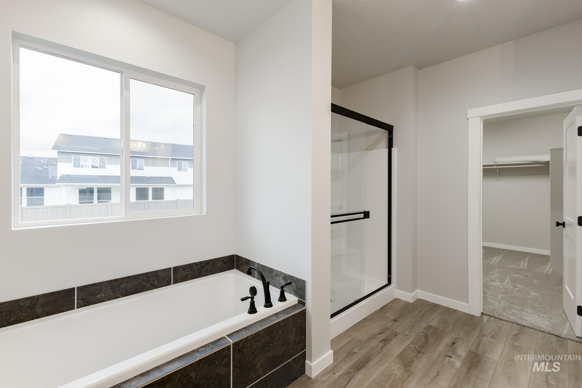 Bathroom featuring a bath, a shower stall, light wood finished floors, and a spacious closet