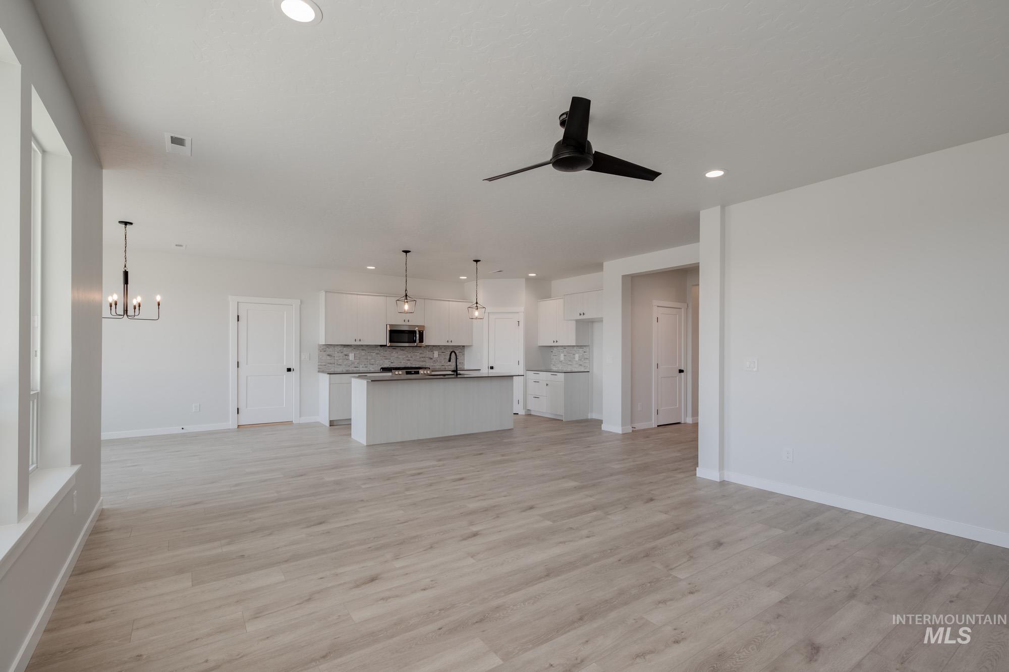 Unfurnished living room with light wood finished floors, recessed lighting, a chandelier, and ceiling fan