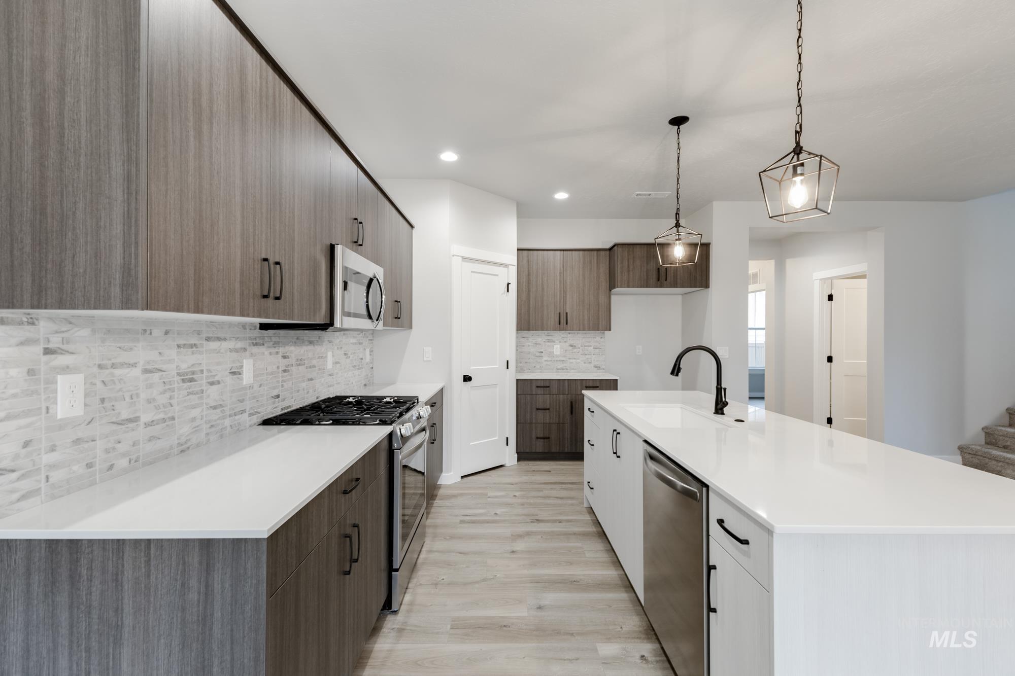 Kitchen with stainless steel appliances, pendant lighting, light wood-style flooring, modern cabinets, and a kitchen island with sink