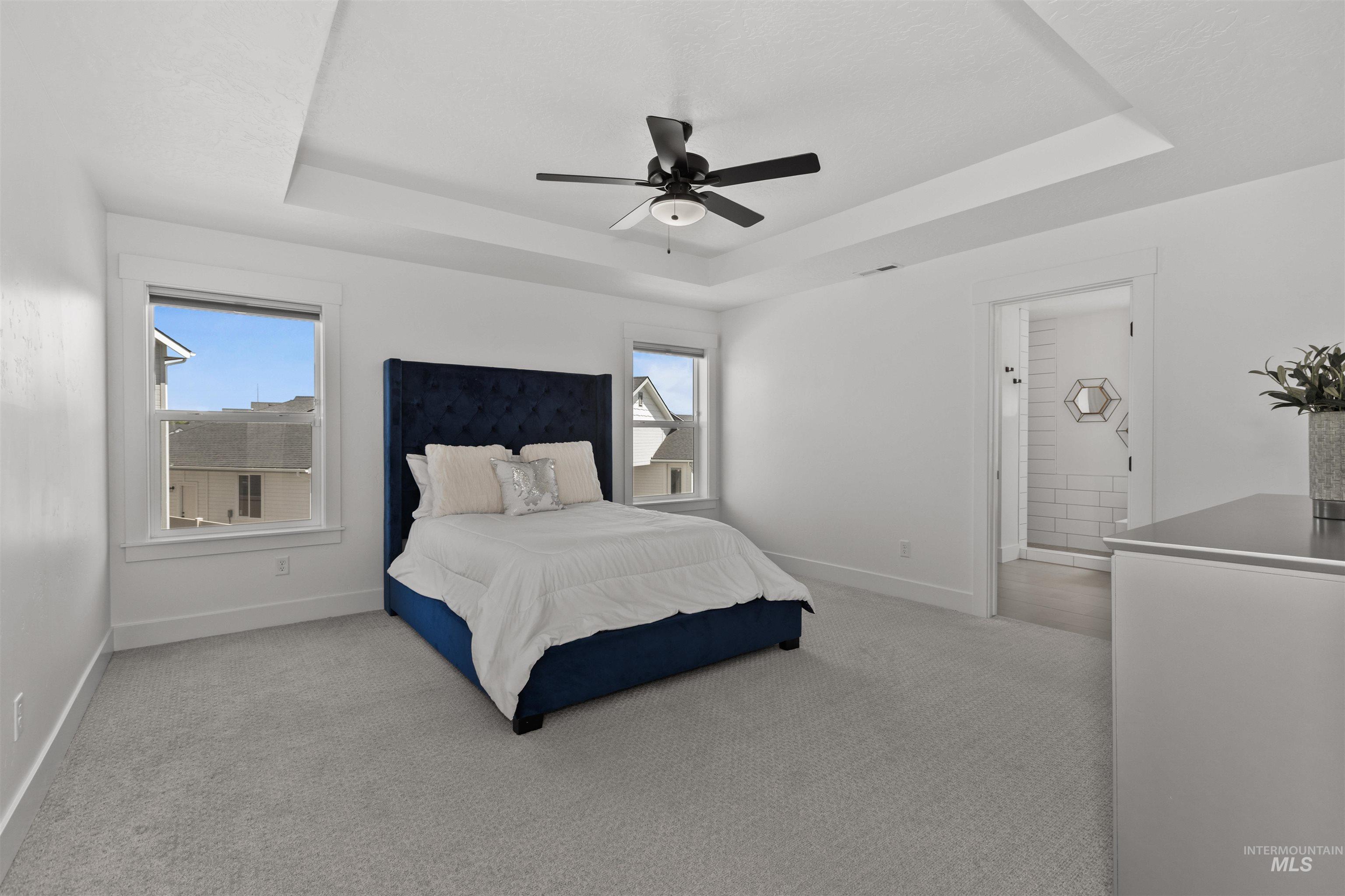 Bedroom featuring a raised ceiling, light colored carpet, and ceiling fan