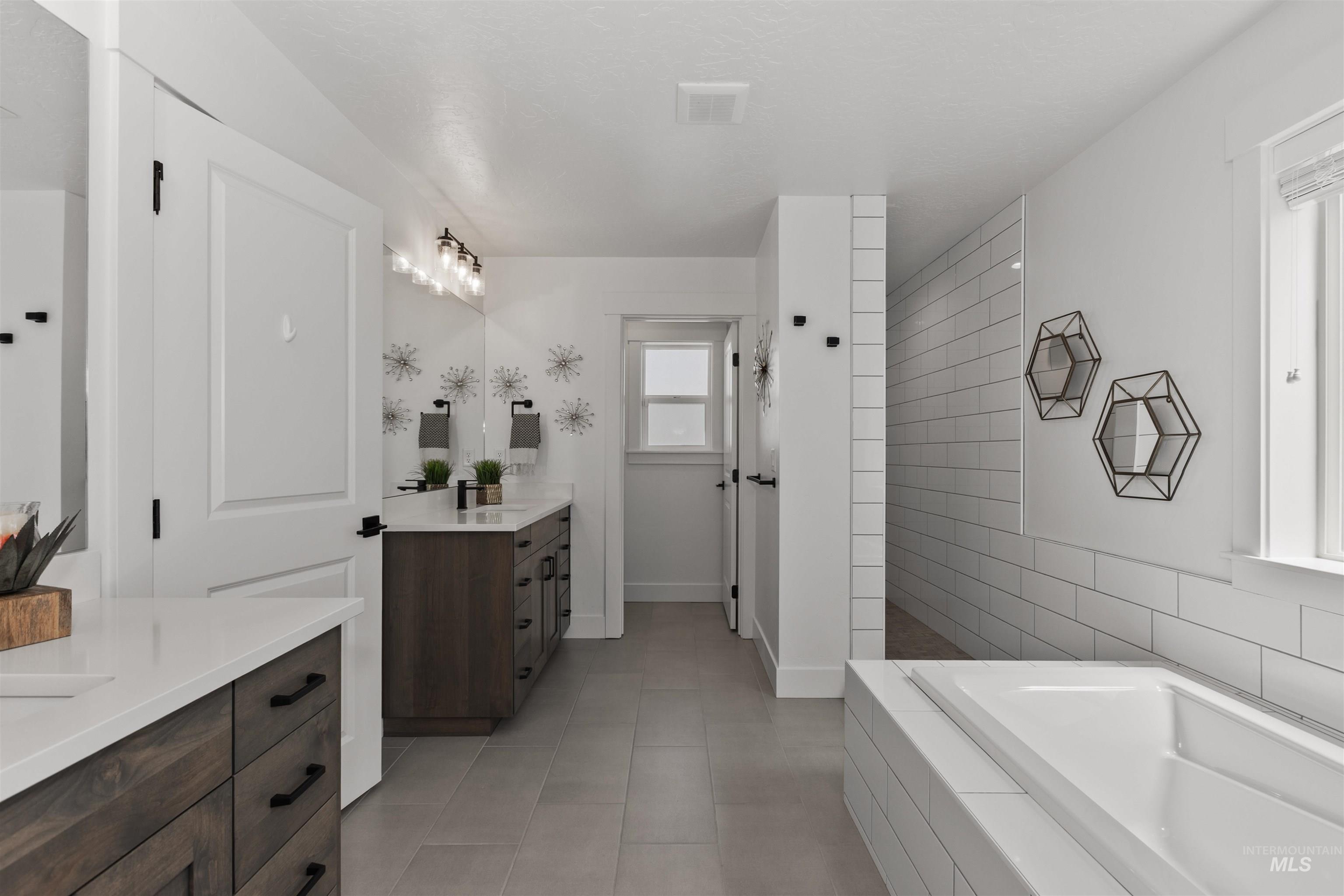 Full bath with two vanities, a bath, walk in shower, light tile patterned floors, and tile walls