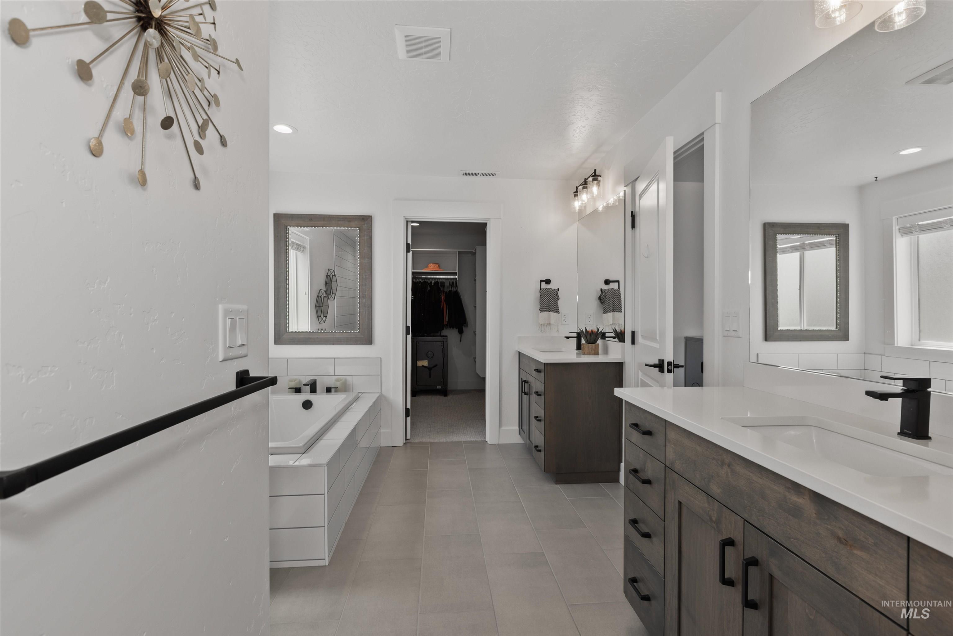 Full bath featuring a walk in closet, two vanities, a bath, and light tile patterned floors