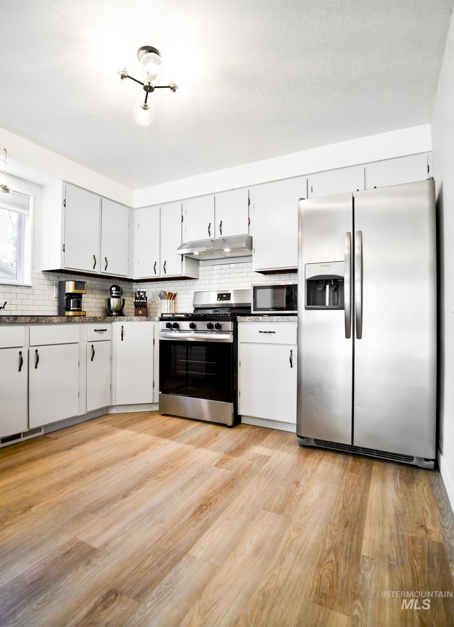 Kitchen featuring stainless steel appliances, light wood-type flooring, tasteful backsplash, and white cabinets
