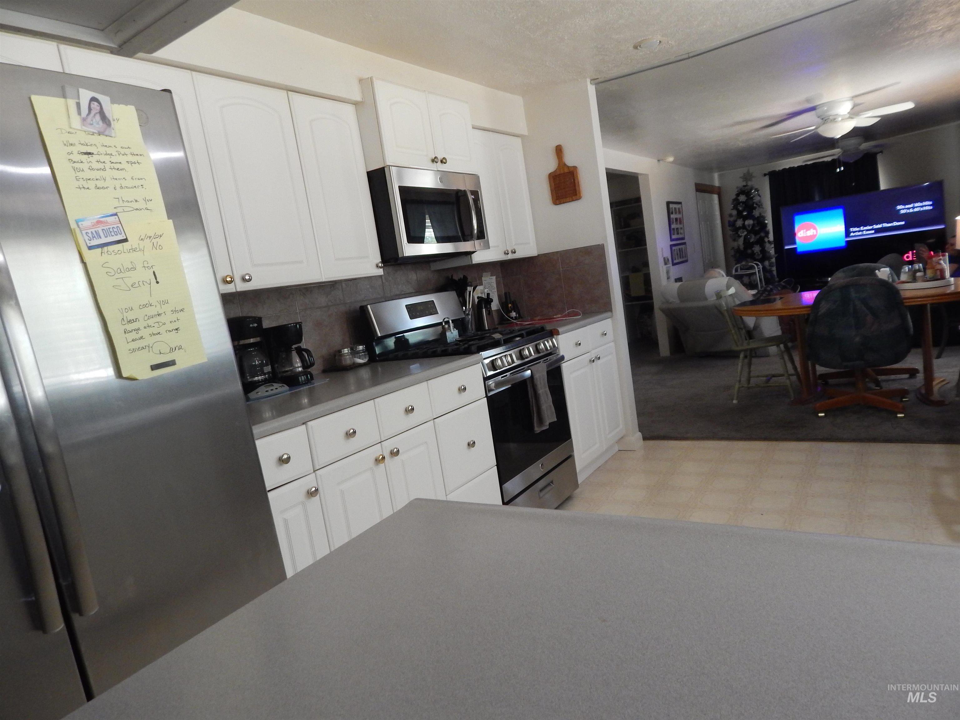 Kitchen featuring stainless steel appliances, ceiling fan, decorative backsplash, and white cabinetry
