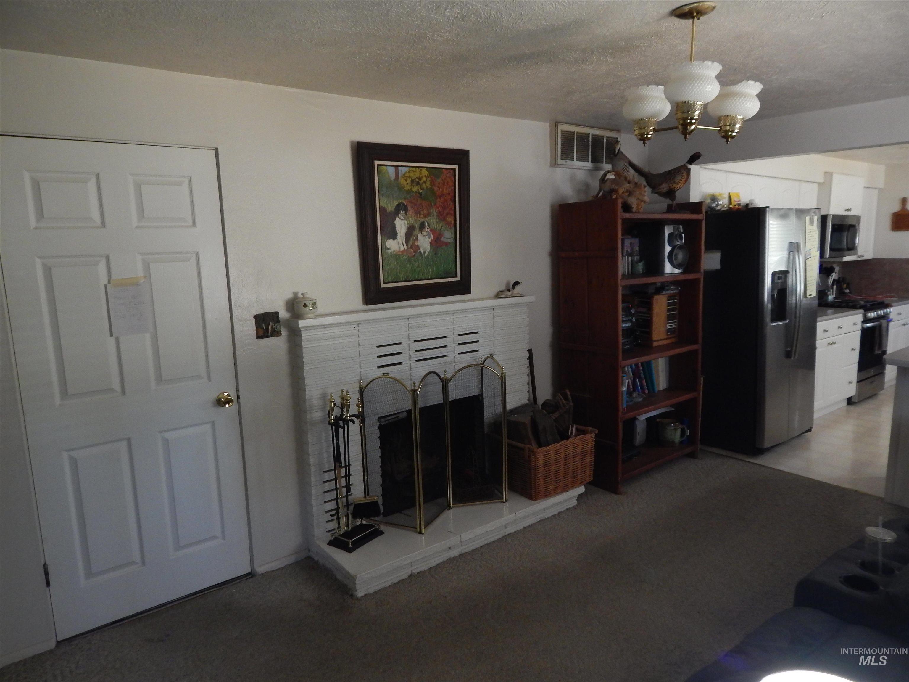 Living area with a chandelier, a brick fireplace, a textured ceiling, and light carpet