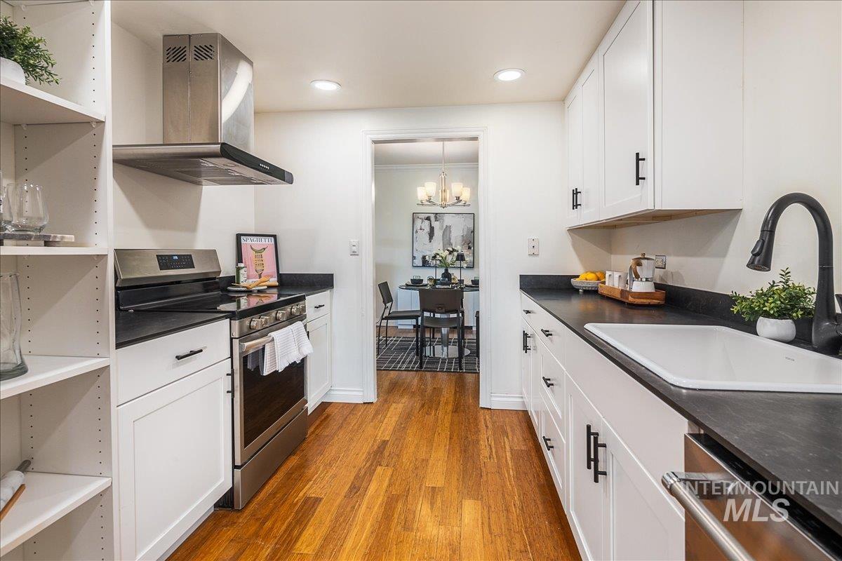 Kitchen featuring dark countertops, open shelves, appliances with stainless steel finishes, extractor fan, and ornamental molding