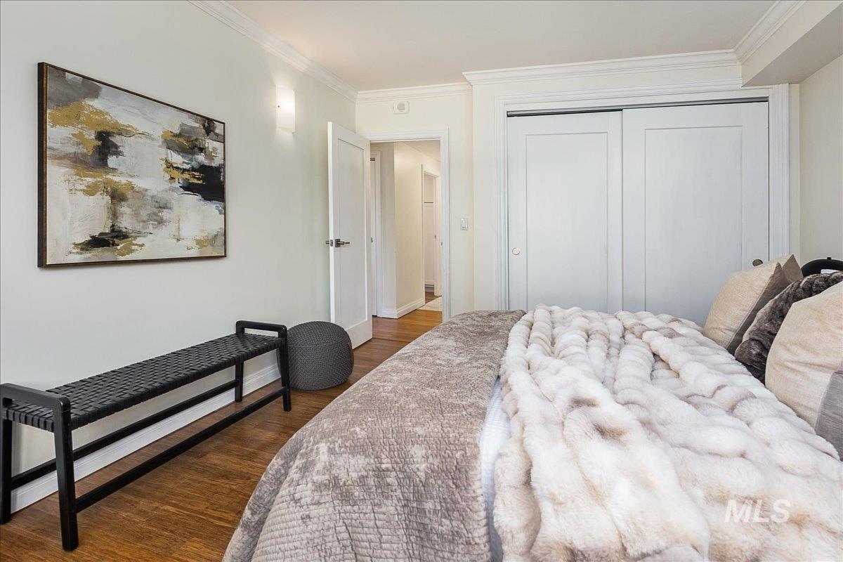 Bedroom with dark wood finished floors, crown molding, and a closet