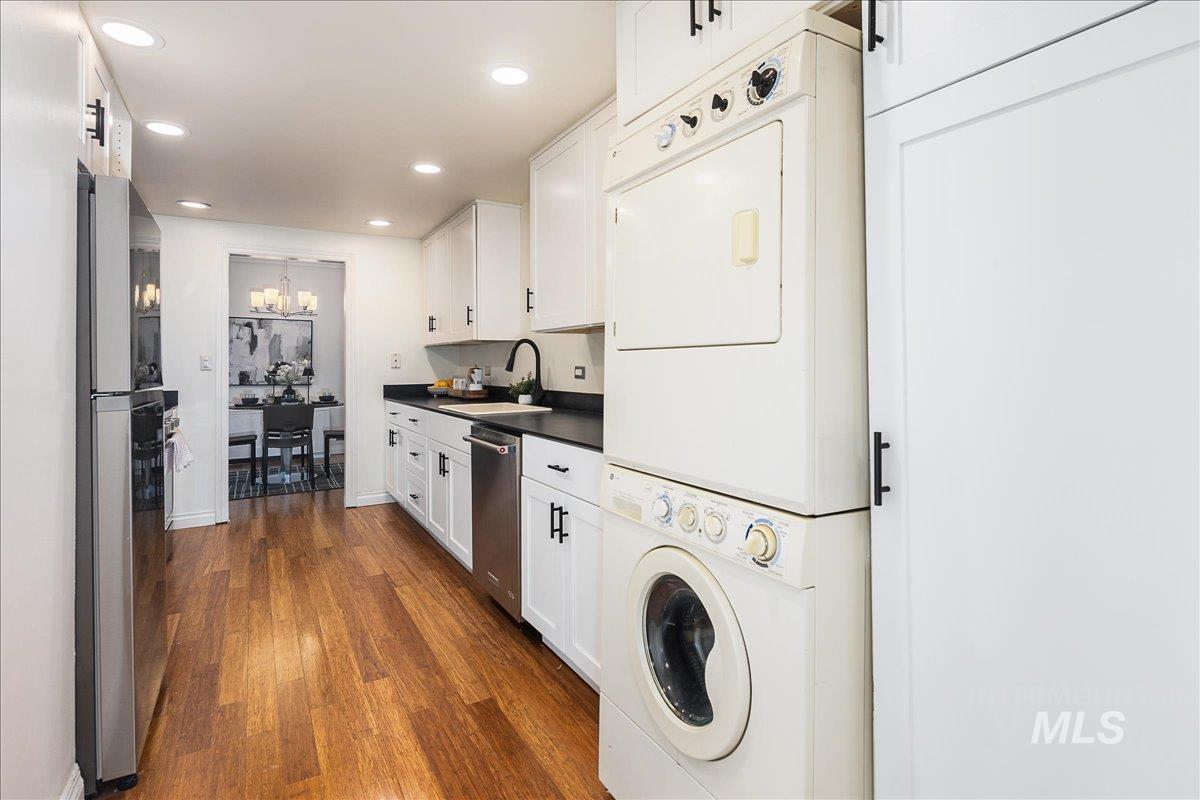 Laundry room featuring dark wood-style flooring, recessed lighting, stacked washer / drying machine, and a chandelier