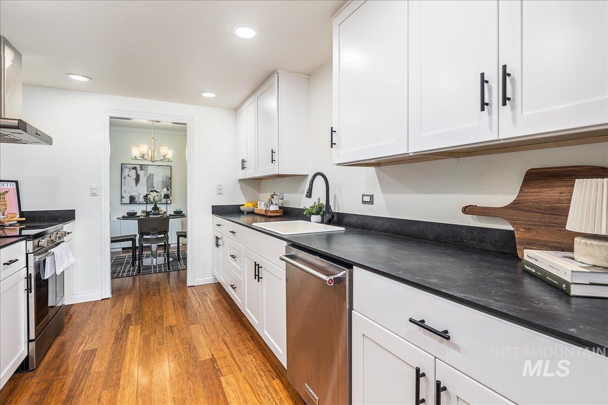 Kitchen with dark countertops, wall chimney exhaust hood, dark wood-style flooring, appliances with stainless steel finishes, and white cabinets