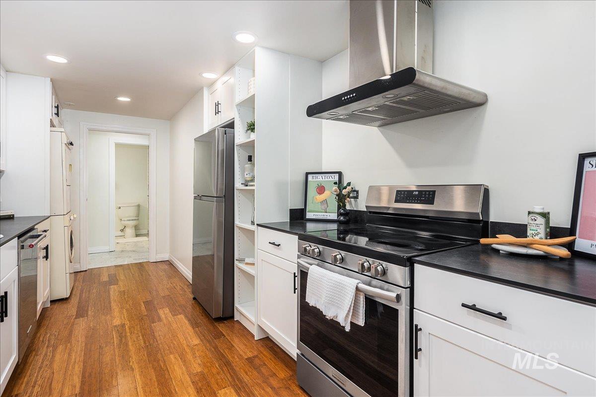 Kitchen featuring appliances with stainless steel finishes, dark countertops, white cabinets, wall chimney exhaust hood, and dark wood-style floors