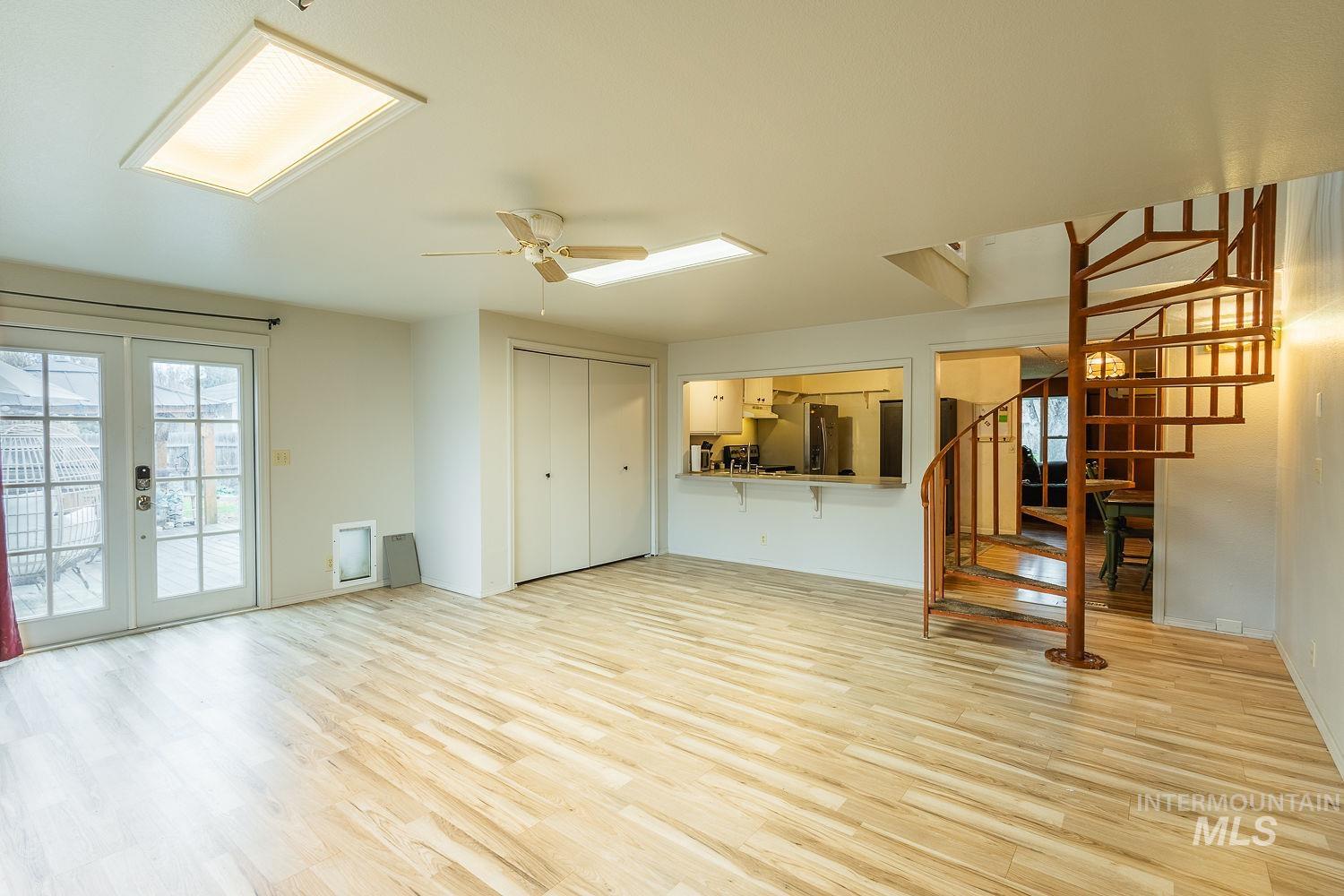 Unfurnished living room featuring french doors, light wood finished floors, ceiling fan, and stairway