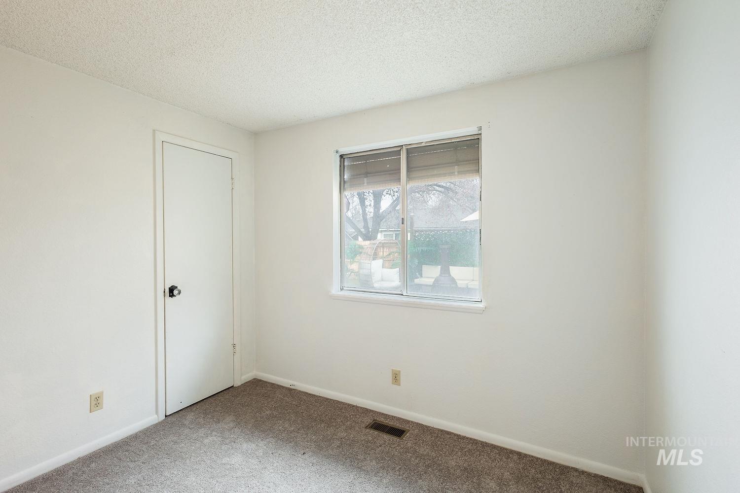 Carpeted empty room with a textured ceiling and baseboards
