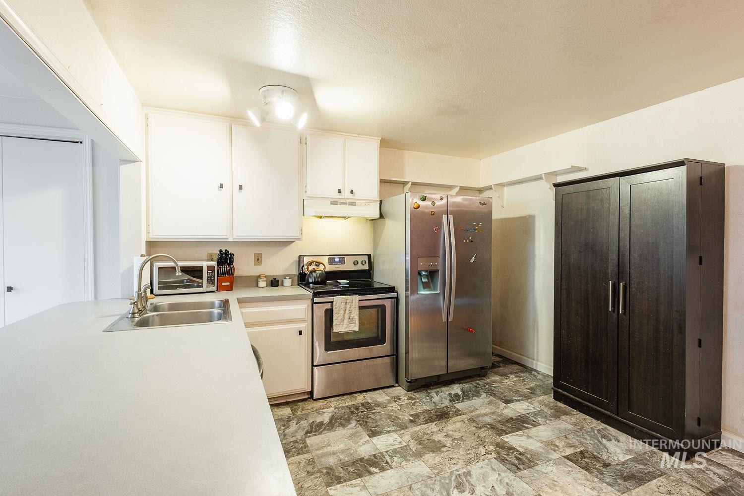 Kitchen featuring stainless steel appliances, light countertops, stone finish floors, under cabinet range hood, and white cabinets