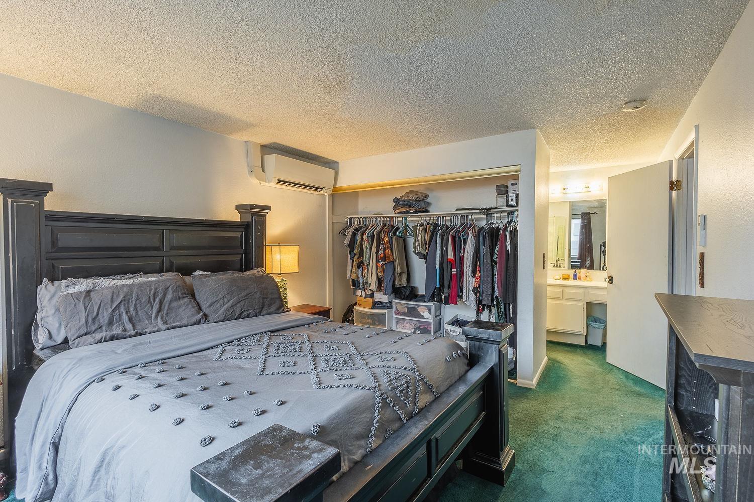 Bedroom with dark colored carpet, a textured ceiling, a closet, and an AC wall unit