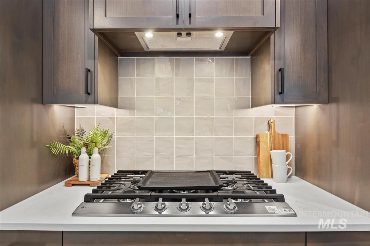 Kitchen view of stainless steel gas stovetop, custom range hood, and tasteful backsplash