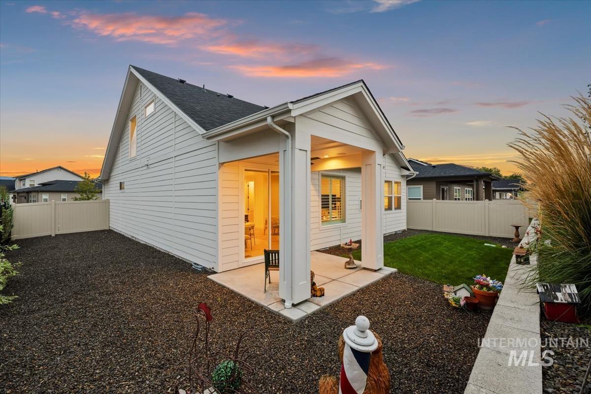 Back of house at dusk featuring a fenced backyard, a patio, and a shingled roof