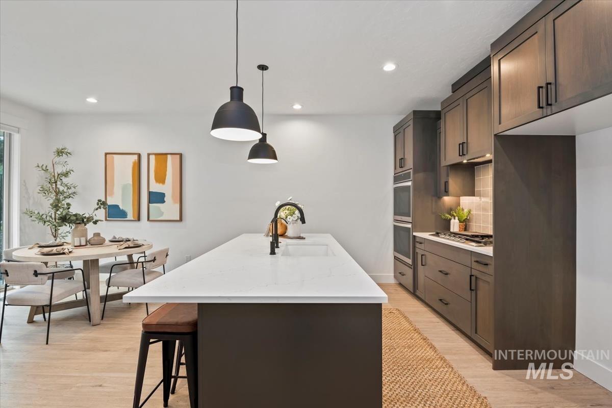 Kitchen featuring pendant lighting, a center island with sink, decorative backsplash, light wood-type flooring, and a kitchen breakfast bar