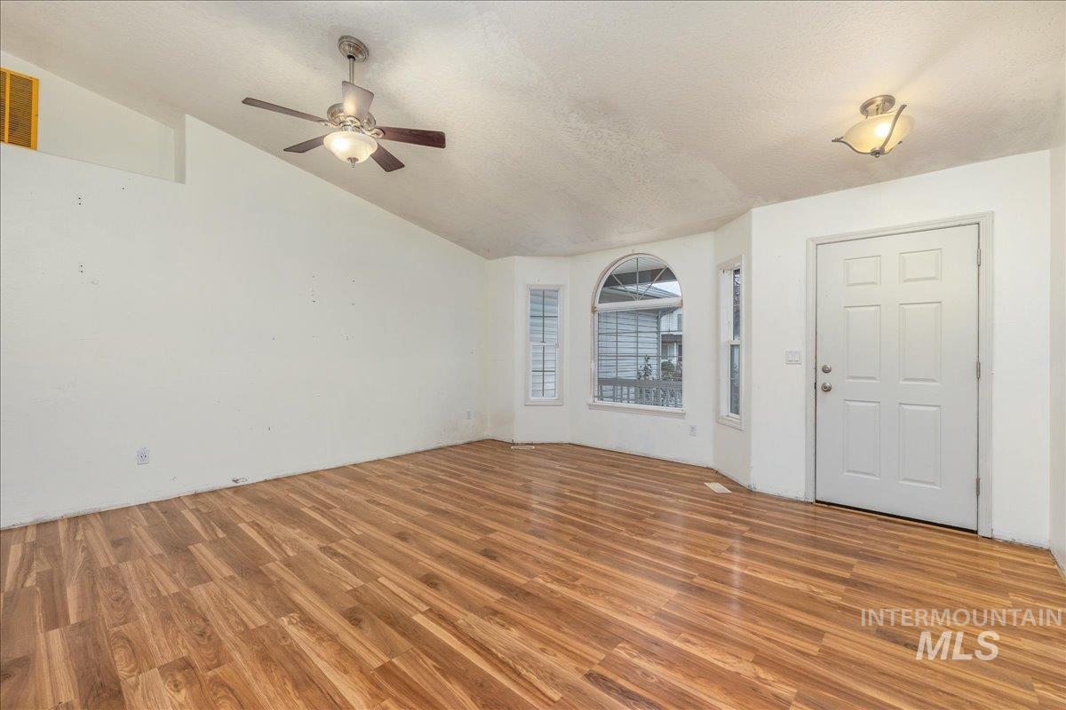 Unfurnished living room featuring wood finished floors, a textured ceiling, lofted ceiling, and a ceiling fan