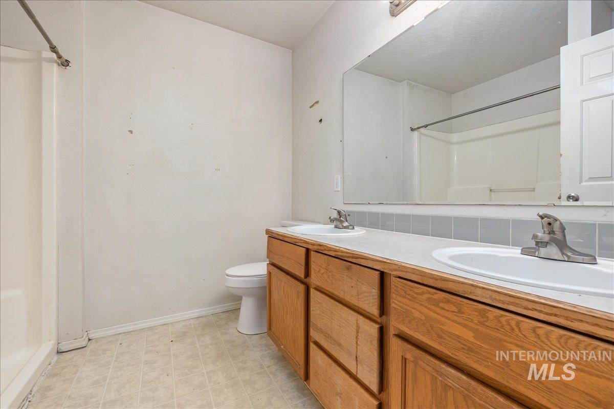 Bathroom with light flooring, double vanity, a shower, and a textured ceiling