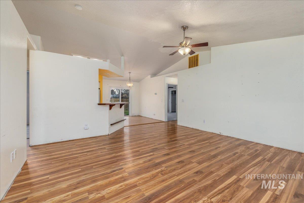 Unfurnished living room featuring light wood finished floors, vaulted ceiling, and ceiling fan