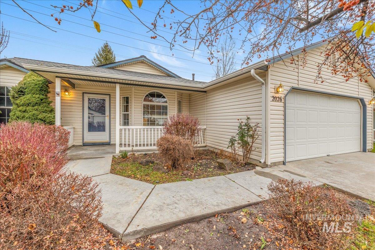 Ranch-style home featuring a porch, a garage, driveway, and a shingled roof